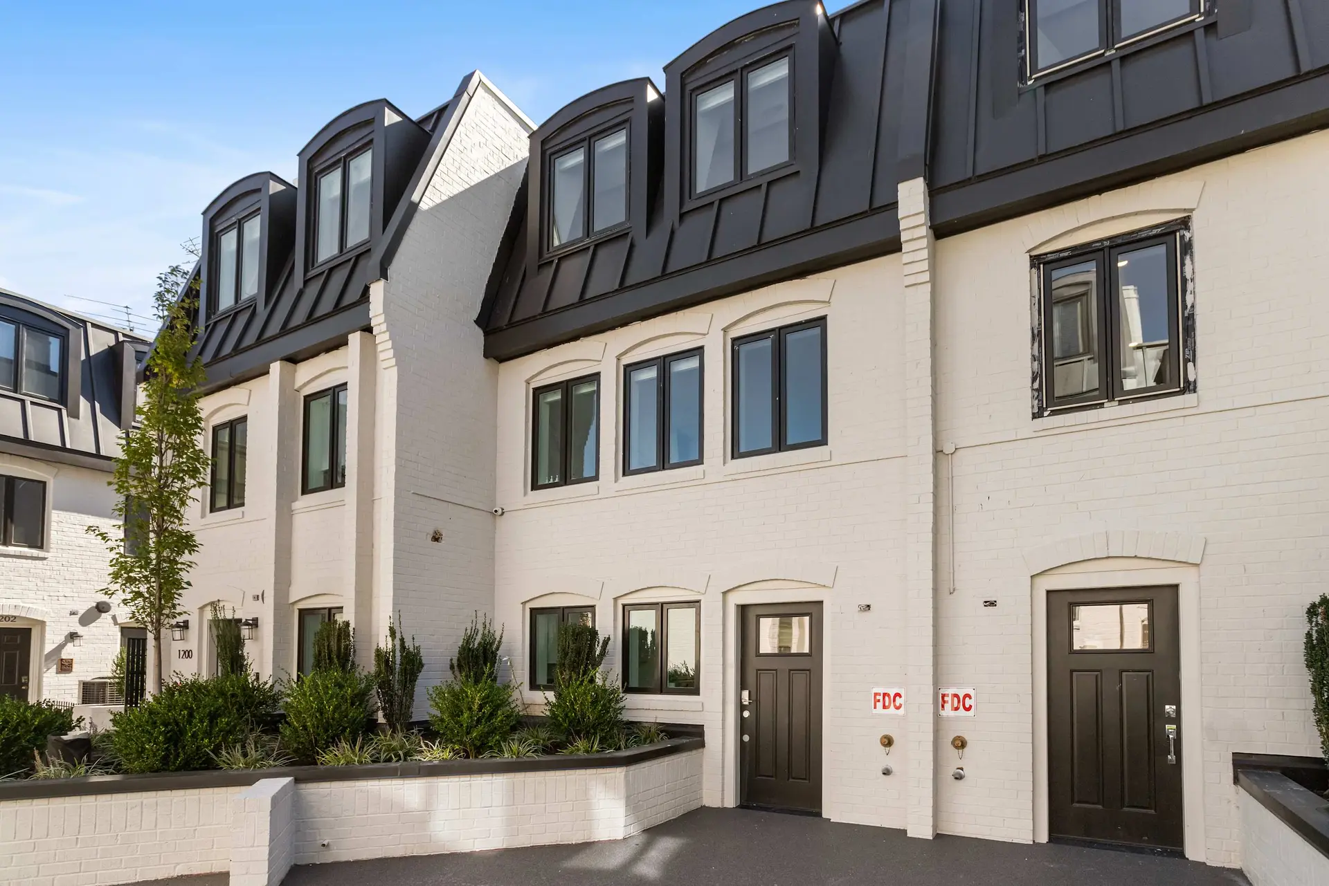 Townhouses with white brick walls, black metal roofs, and dormer windows.