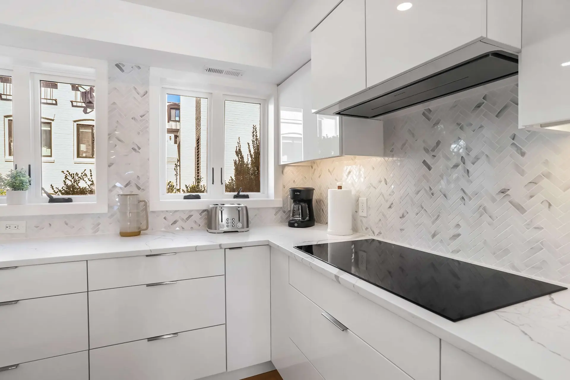 Modern white kitchen with marble backsplash and countertop, stainless steel appliances, and ample na