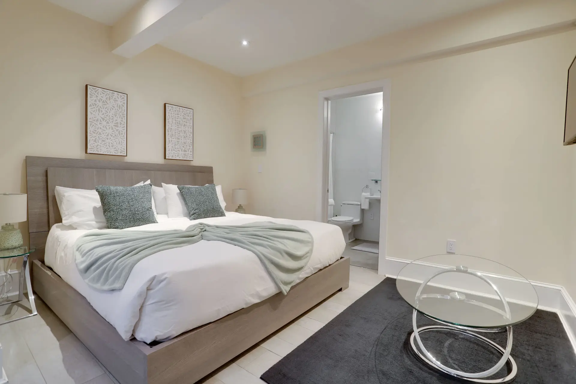 A bedroom with a large bed, two decorative pillows, a light blue throw, and a bathroom with a toilet