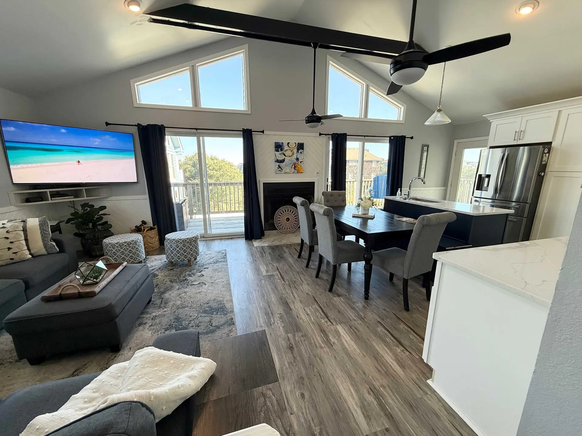 A spacious living room and kitchen area with a vaulted ceiling, large windows, and modern furnishing