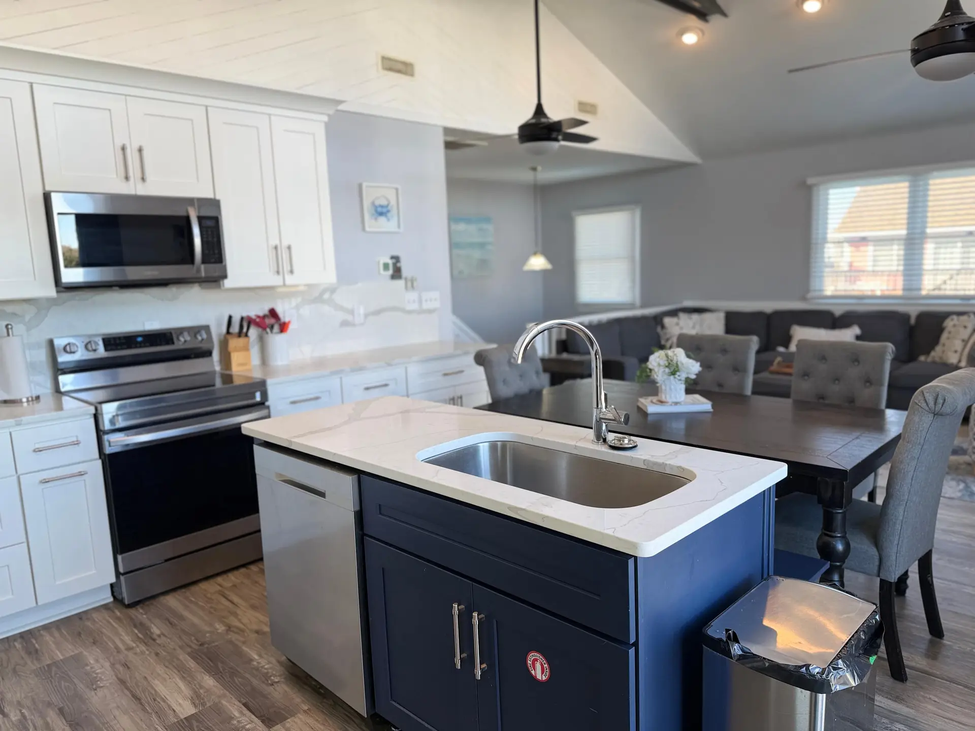 Modern kitchen with white cabinets, stainless steel appliances, and a navy blue island with a sink.
