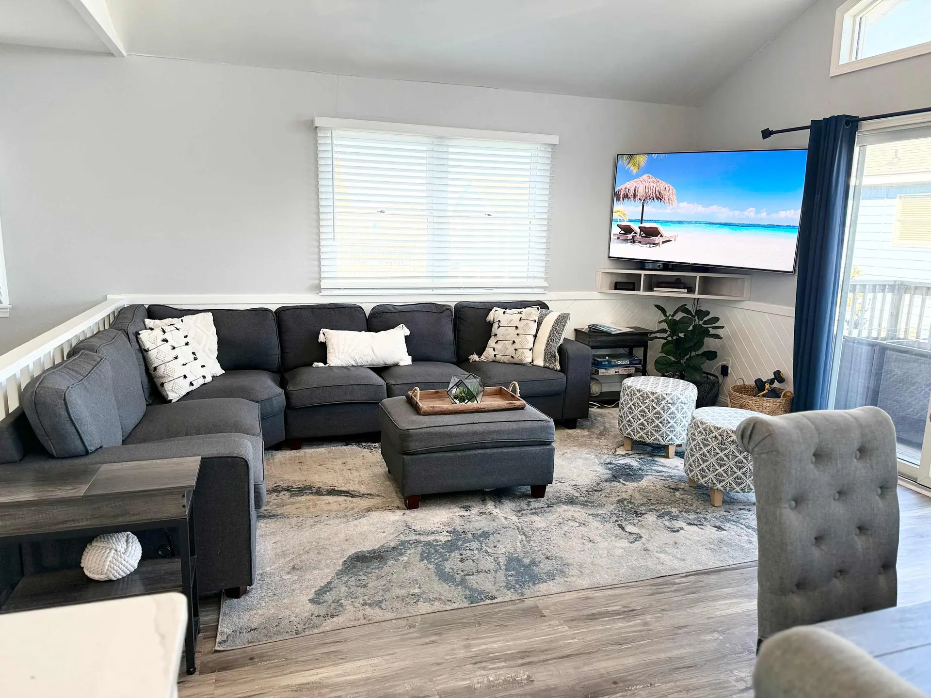 Living room with a large sectional sofa, ottoman, and TV displaying a beach scene.