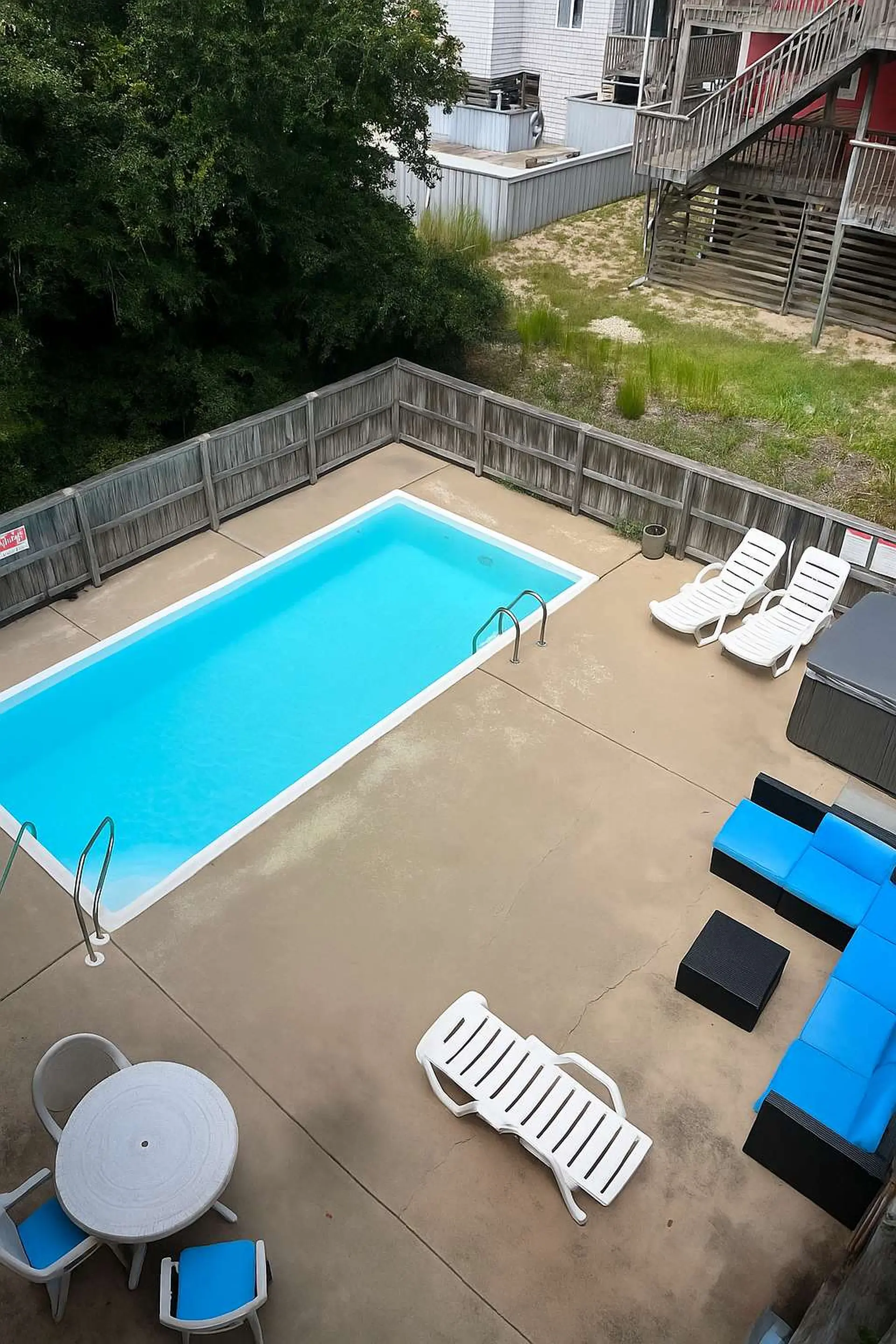 An aerial view of a fenced in pool area with lounge chairs, a table and chairs, and a hot tub.