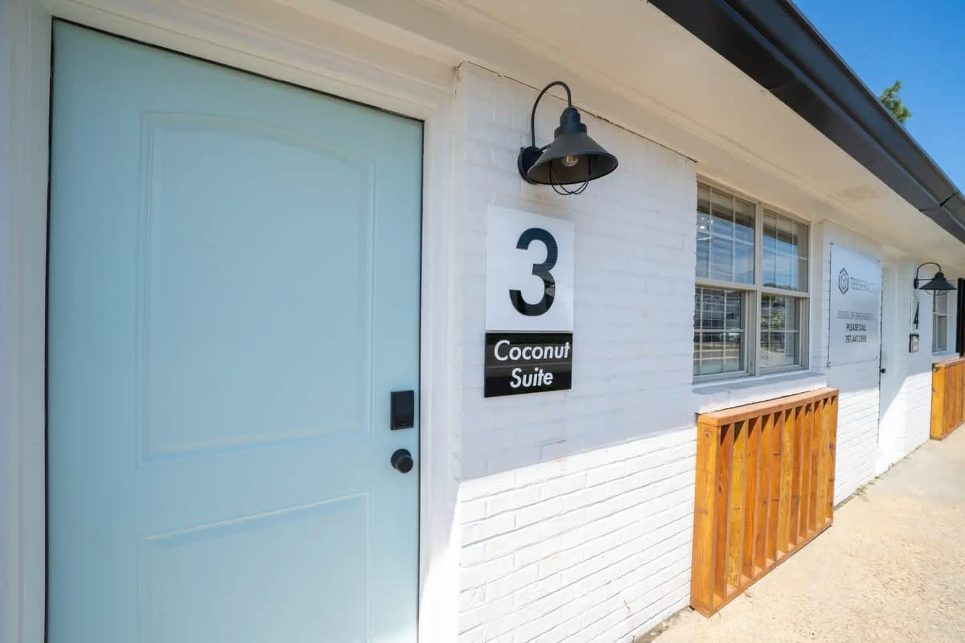 A light blue door with a black handle, next to a white brick wall with a sign for "Coconut Suite 3".