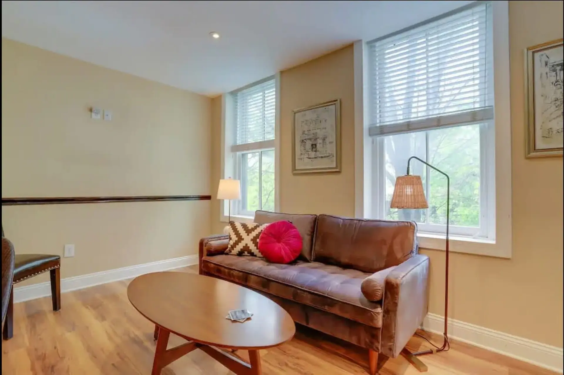 A cozy living room with a brown sofa, coffee table, and two windows.