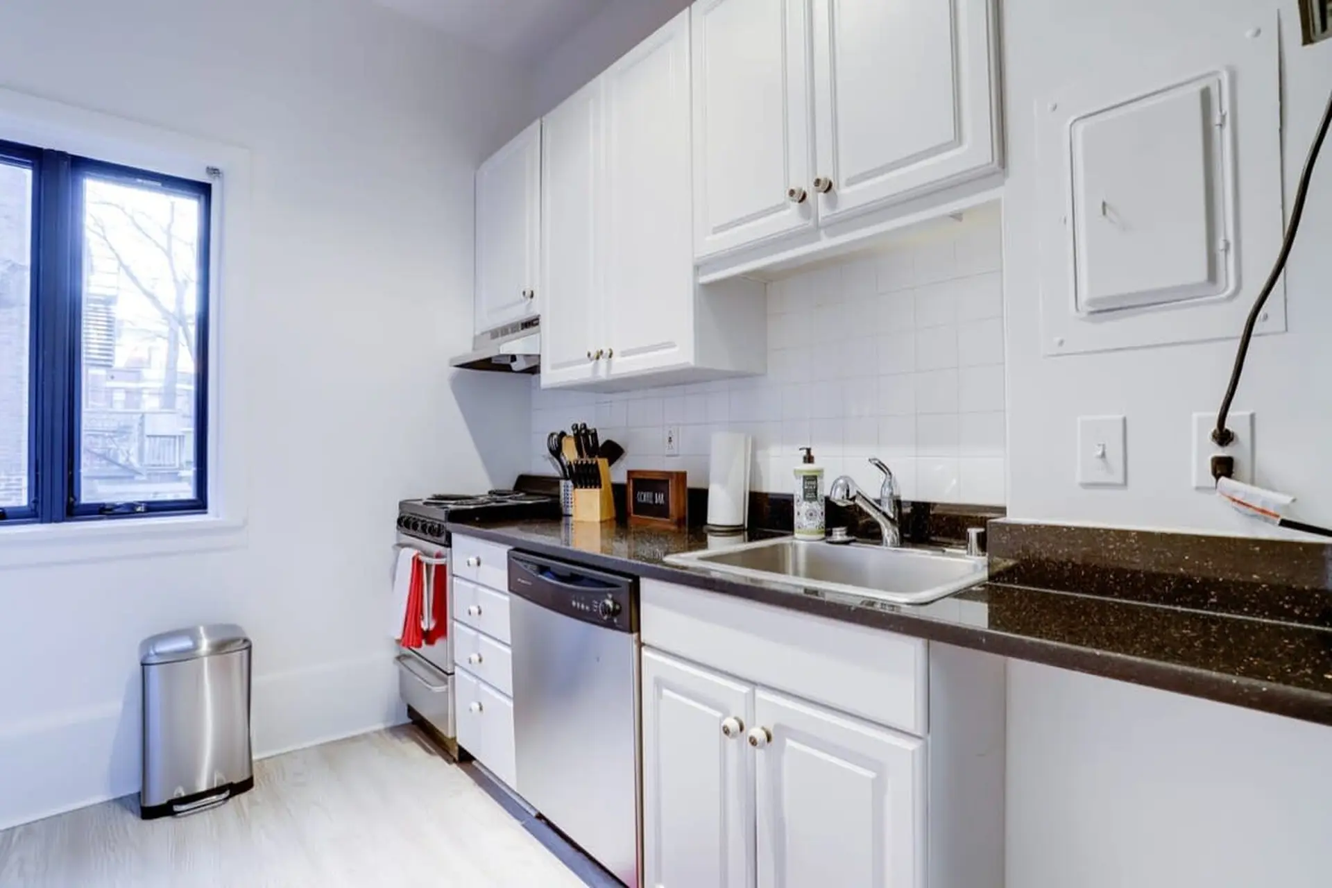 A compact kitchen with white cabinets, a stainless steel sink, dishwasher, and stove.