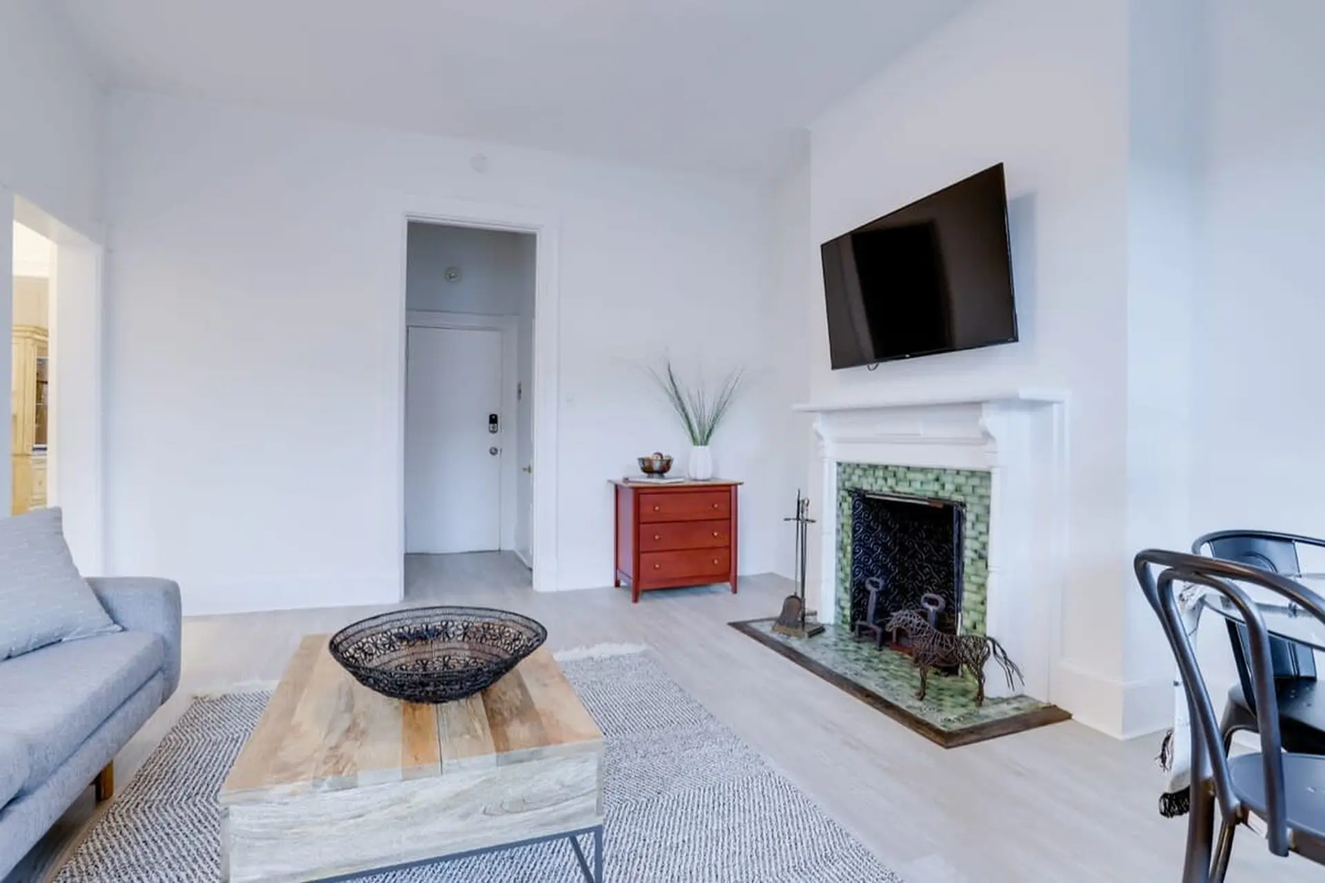 A living room features a grey sofa, a wooden coffee table, and a fireplace with a mounted TV.