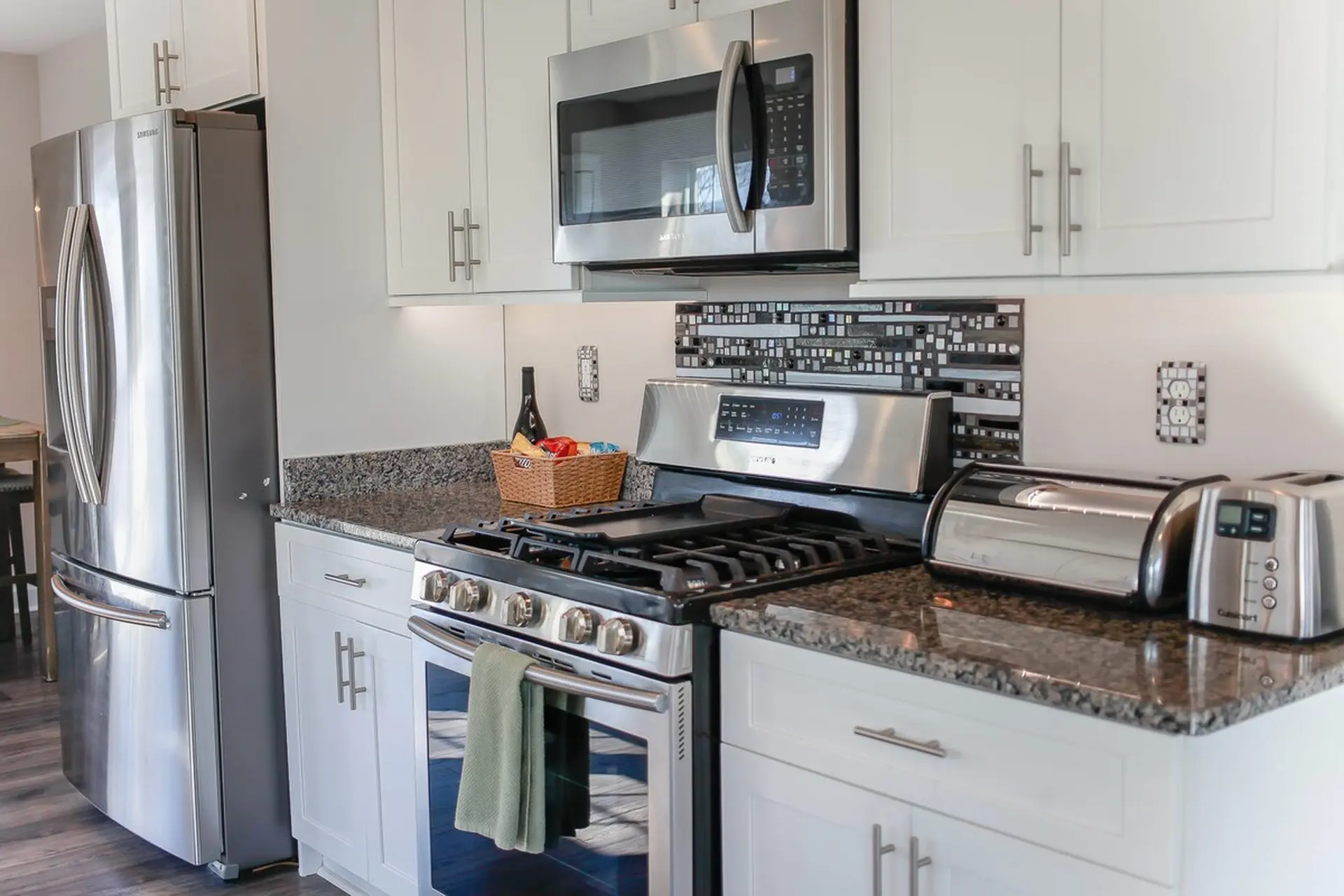A stainless steel kitchen with white cabinets, appliances, and granite countertops.