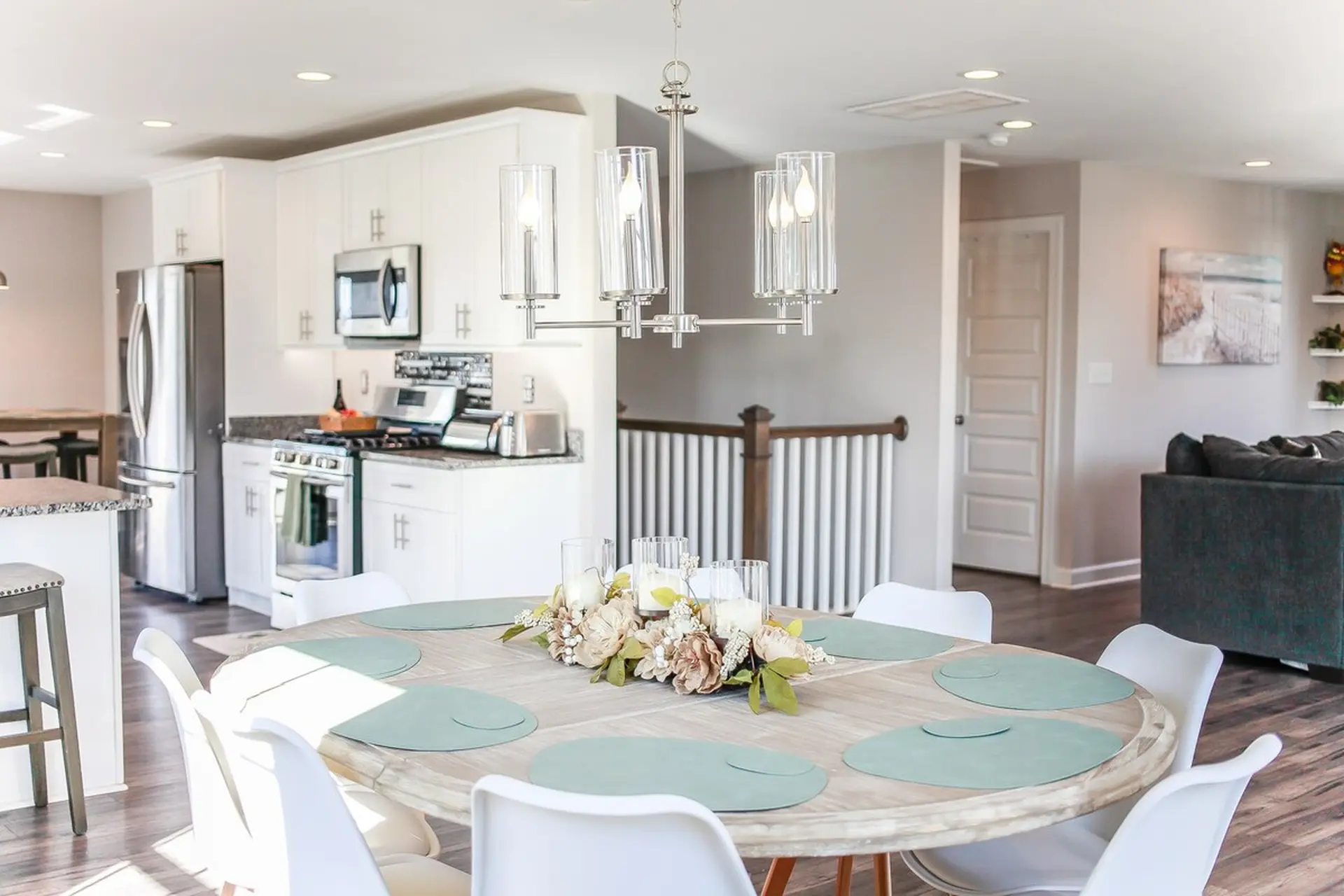 A dining table with light blue placemats and a floral centerpiece is surrounded by white chairs.