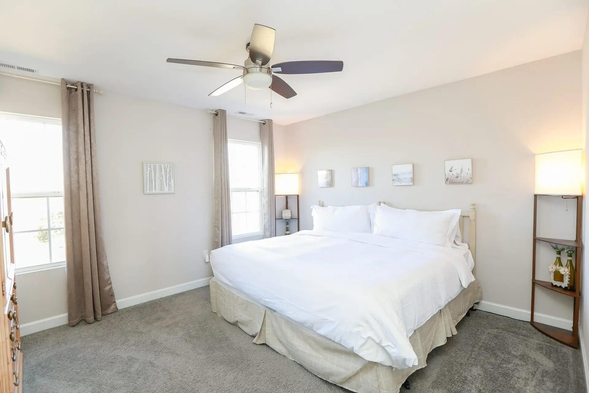 A bedroom with a king-size bed, two windows, a ceiling fan, and a floor lamp.
