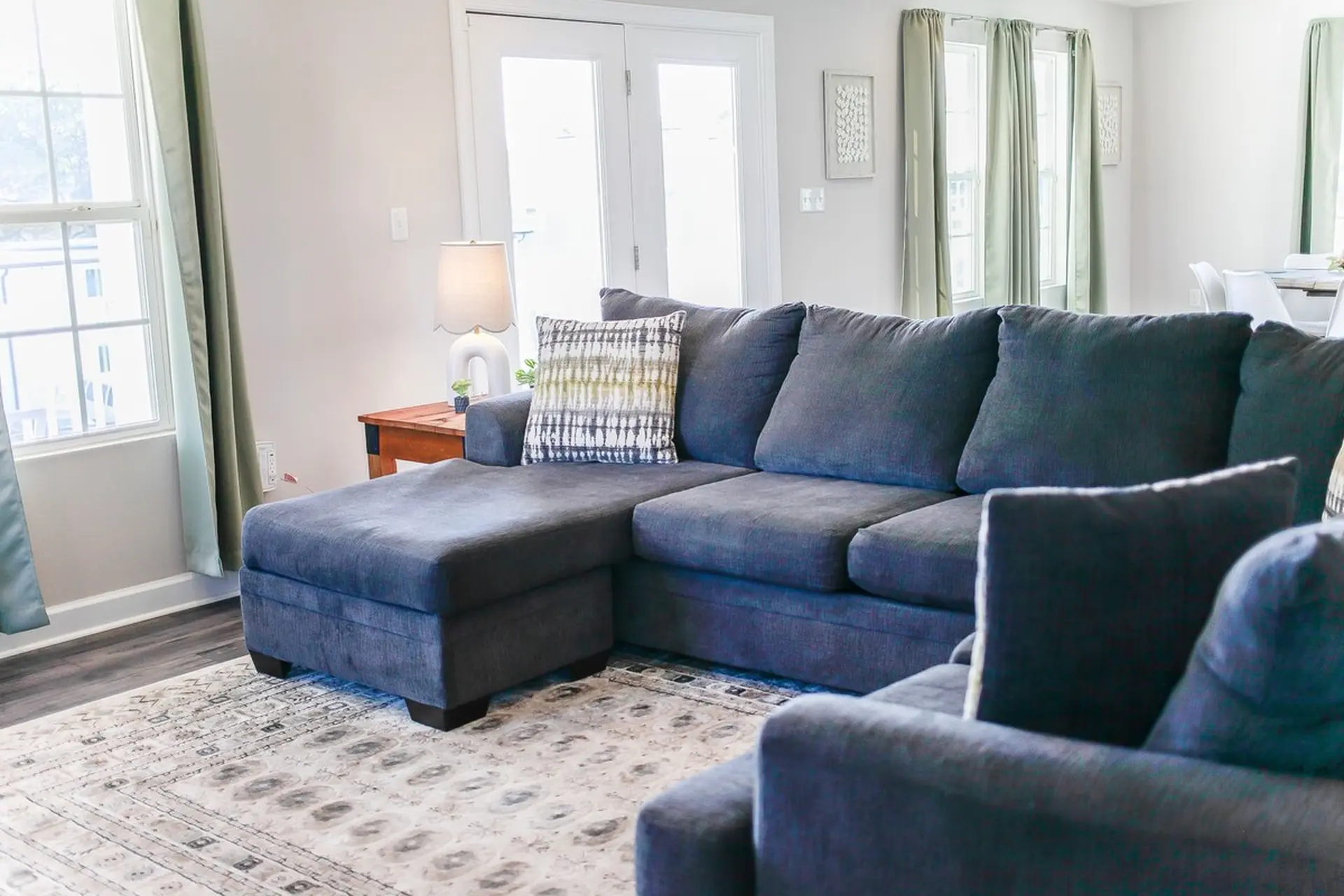 A sectional sofa in a living room with a patterned rug and green curtains.