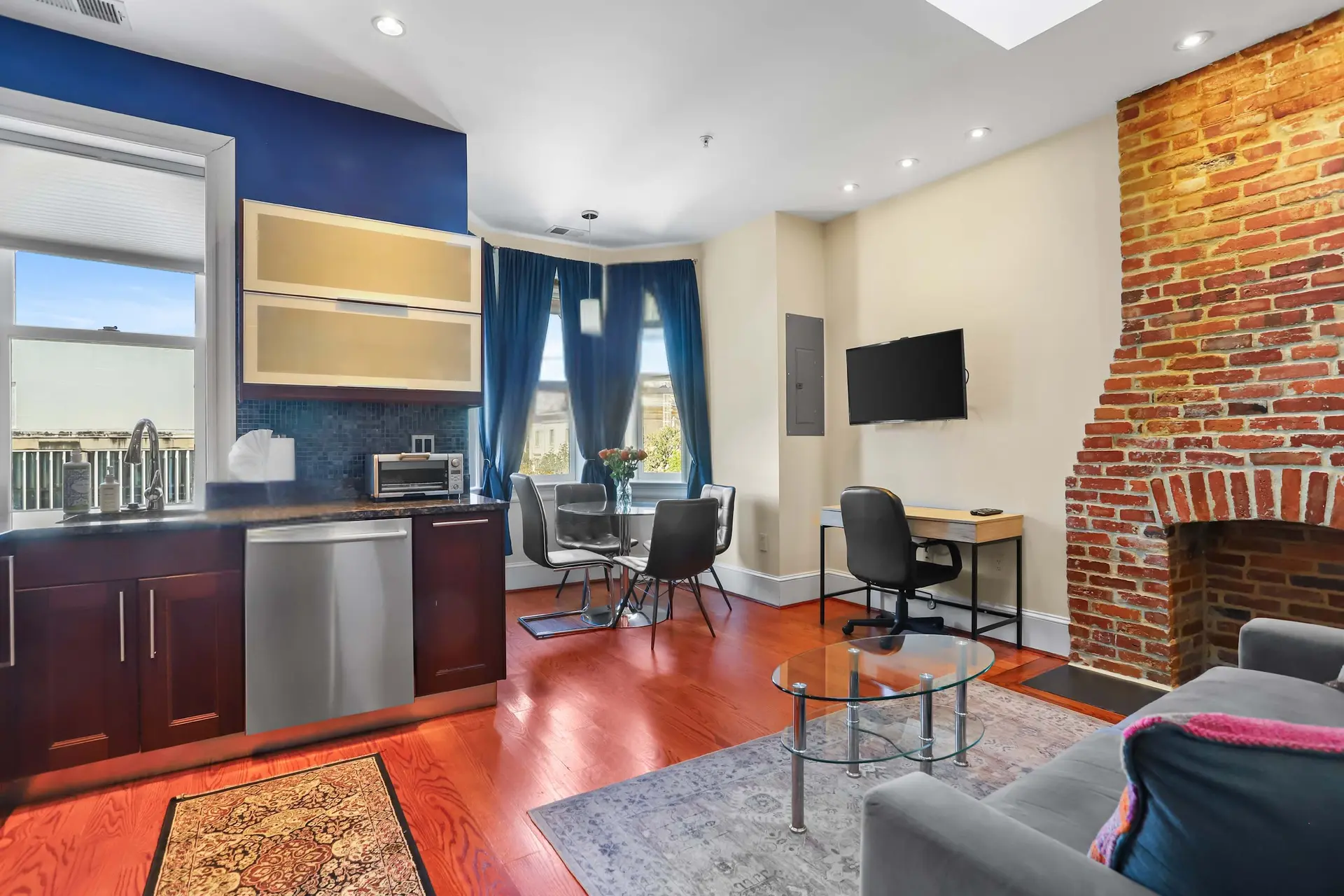 Living room with a sectional couch, brick fireplace, and a desk.