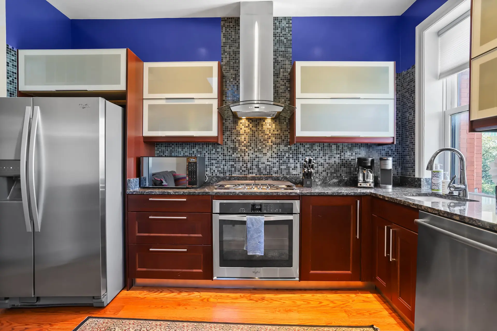 A modern kitchen with blue walls, cherry wood cabinets, and stainless steel appliances.
