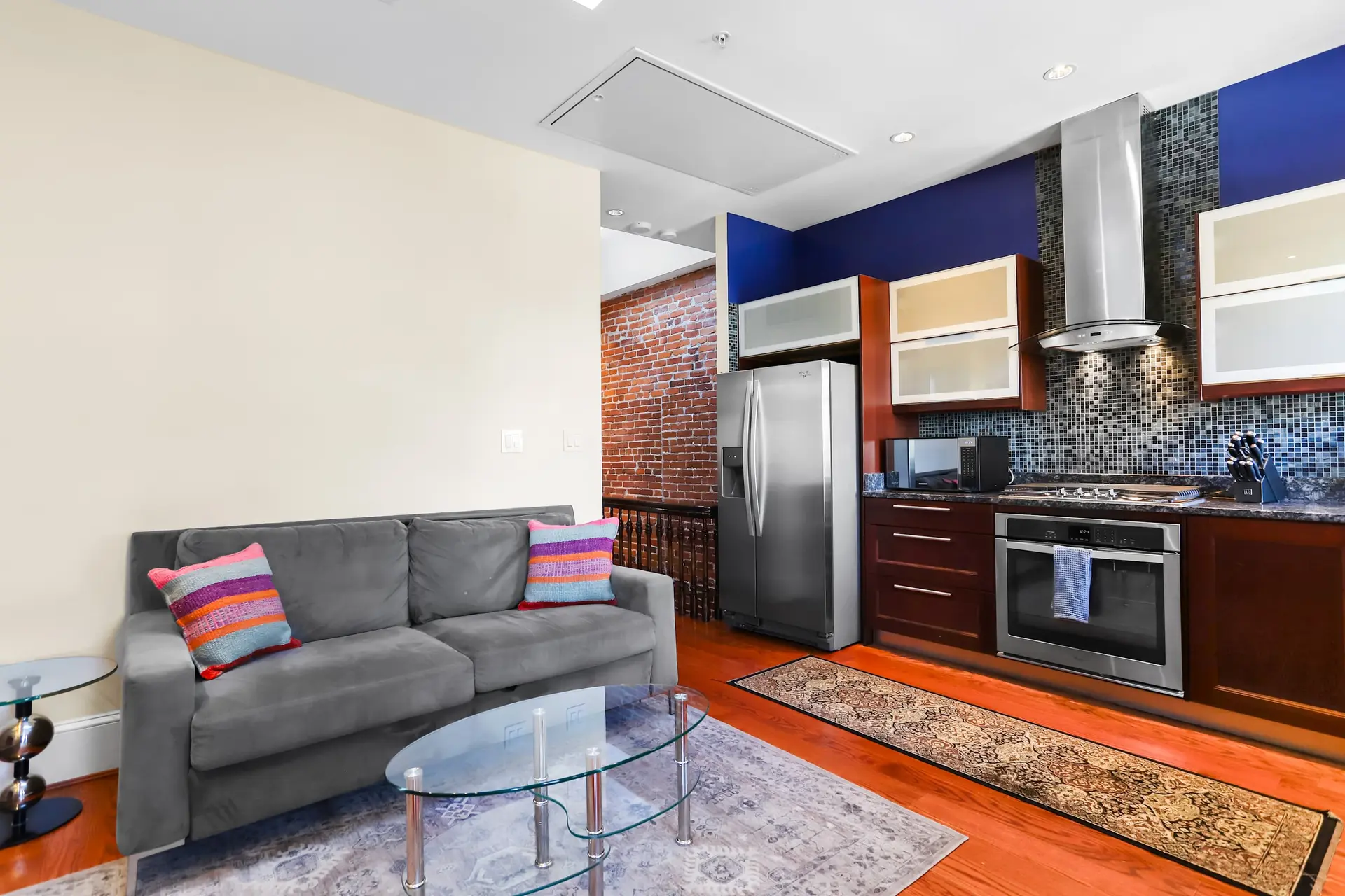 Sleek modern kitchen and living area with gray sofa, glass coffee table, and stainless steel applian