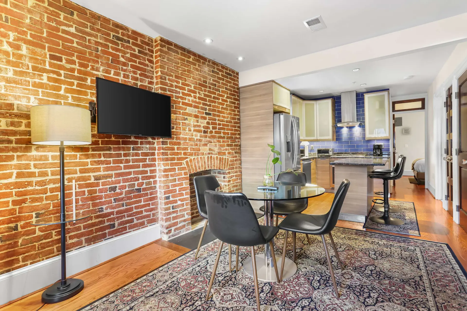 A dining table with chairs is set on a Persian rug in front of exposed brick walls.