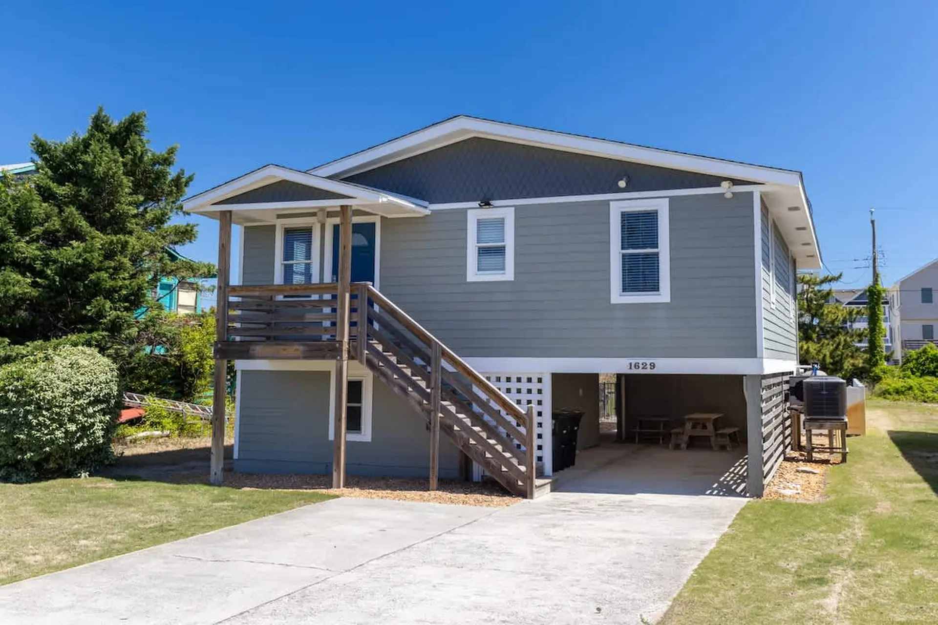 A two-story gray beach house with a wooden deck and stairs.