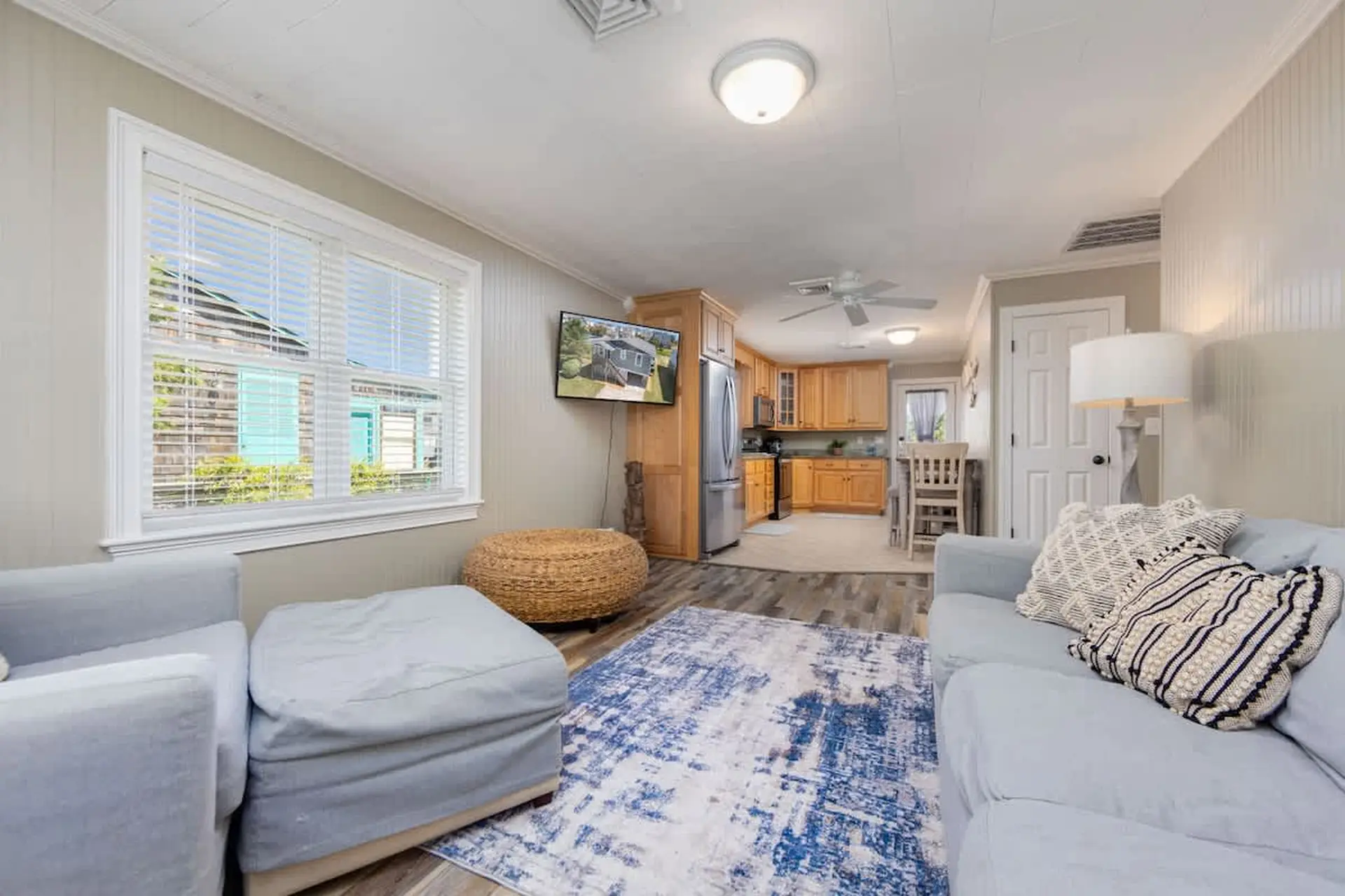 Light blue couch with patterned pillows and a blue and white rug in a living room with a kitchen vie