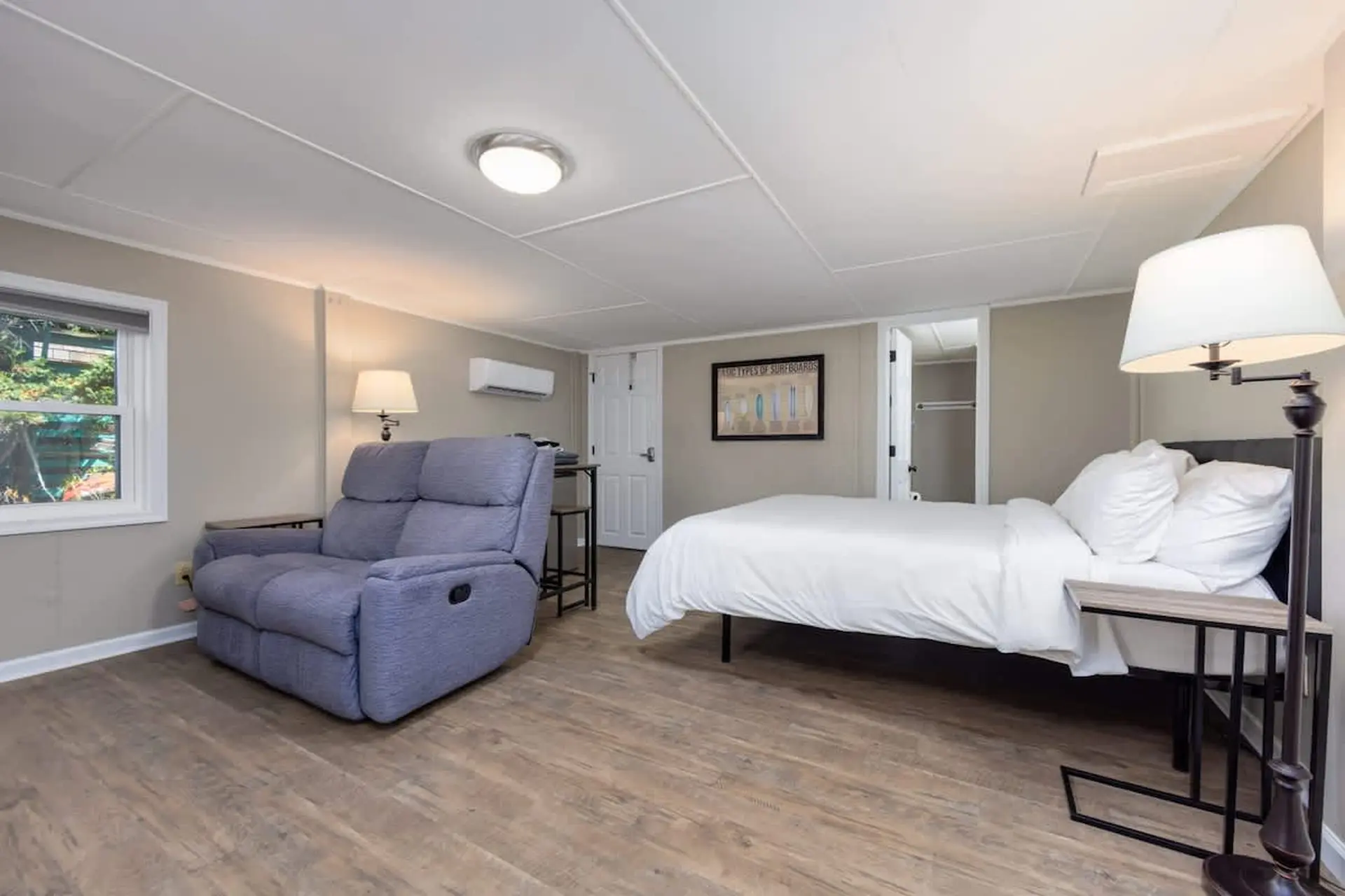 Bedroom with a recliner, bed, and a surf board poster on the wall.