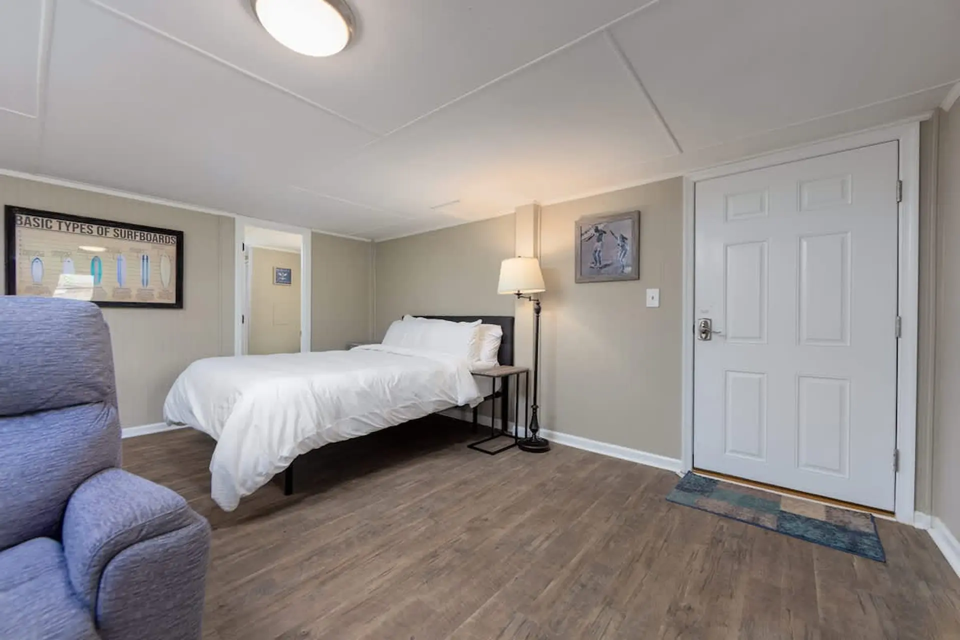 A bedroom with a white bed, blue chair, and a white door.