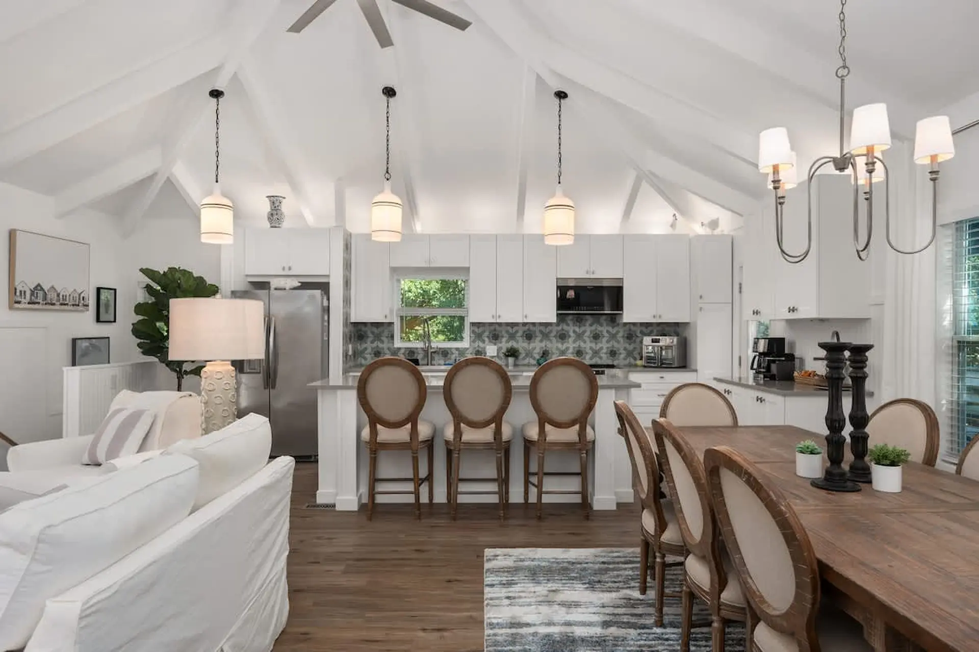 Living room and kitchen with white cabinets, island, dining table and chairs.