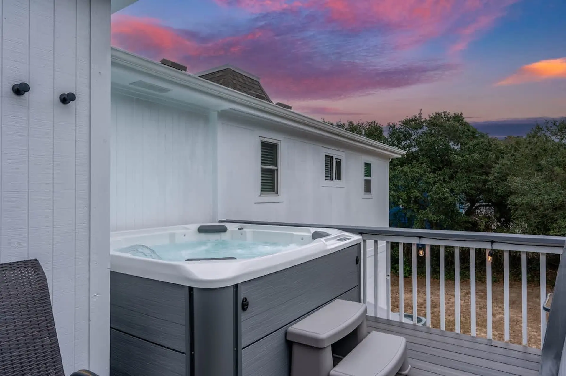 A modern hot tub sits on a deck with a colorful sunset sky in the background.