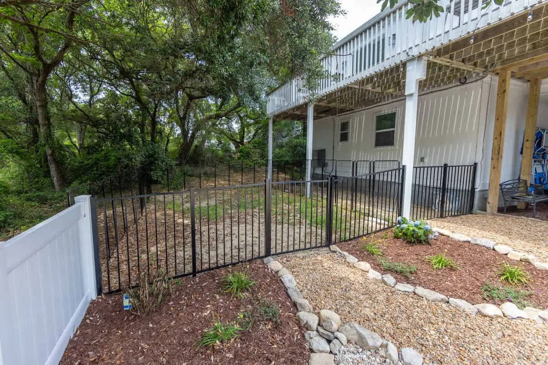 A fenced backyard with a raised deck and lush trees.