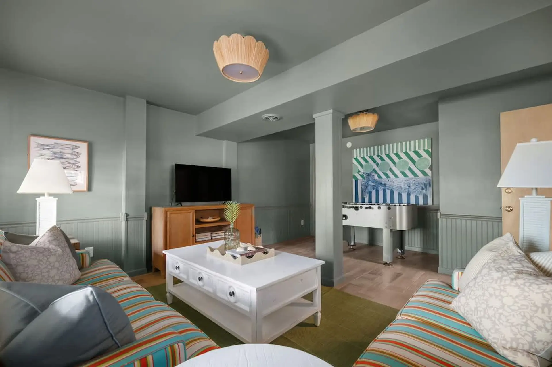 A living room with a foosball table, colorful striped sofas, and a white coffee table.