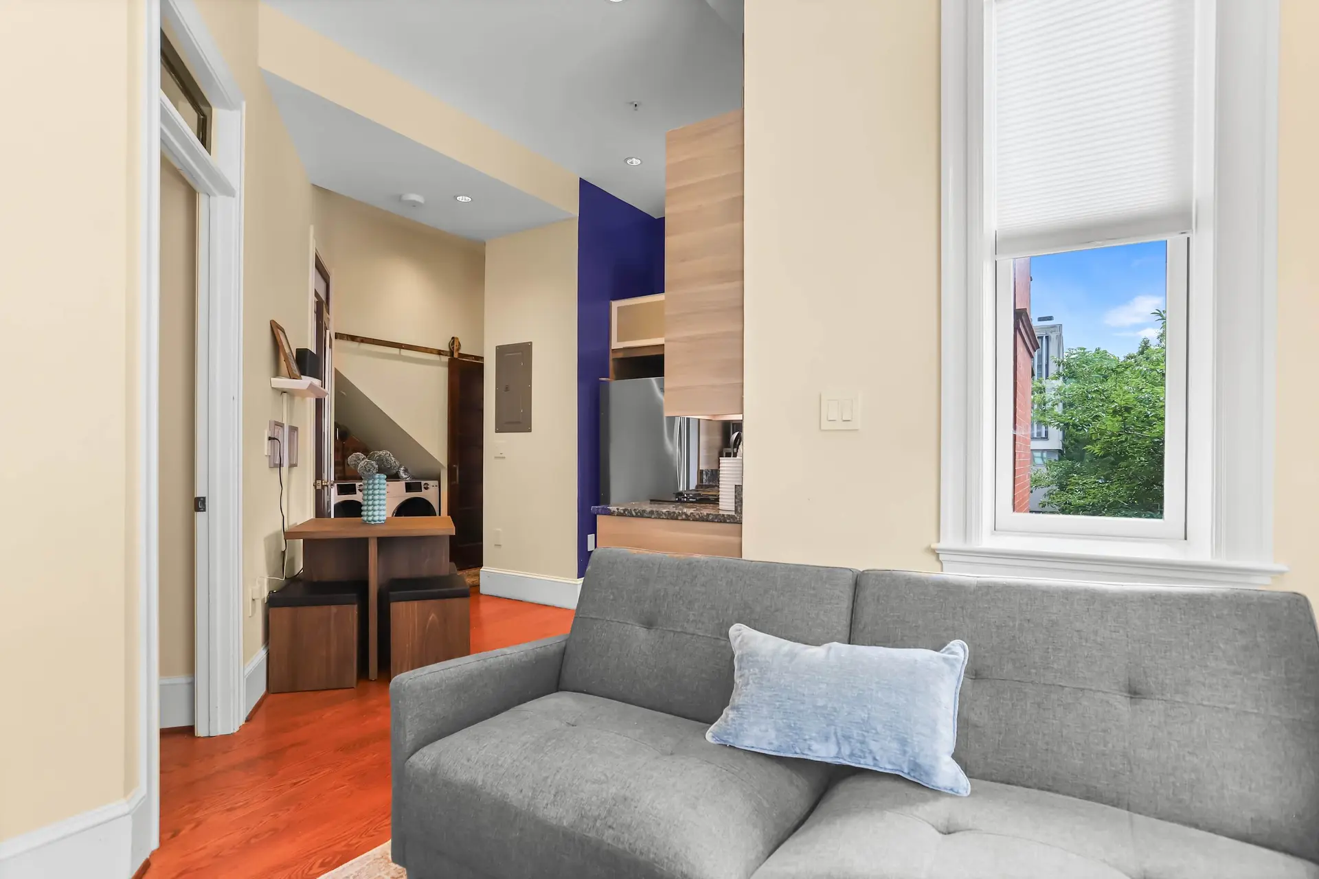 A grey couch with a blue pillow sits in front of a window.