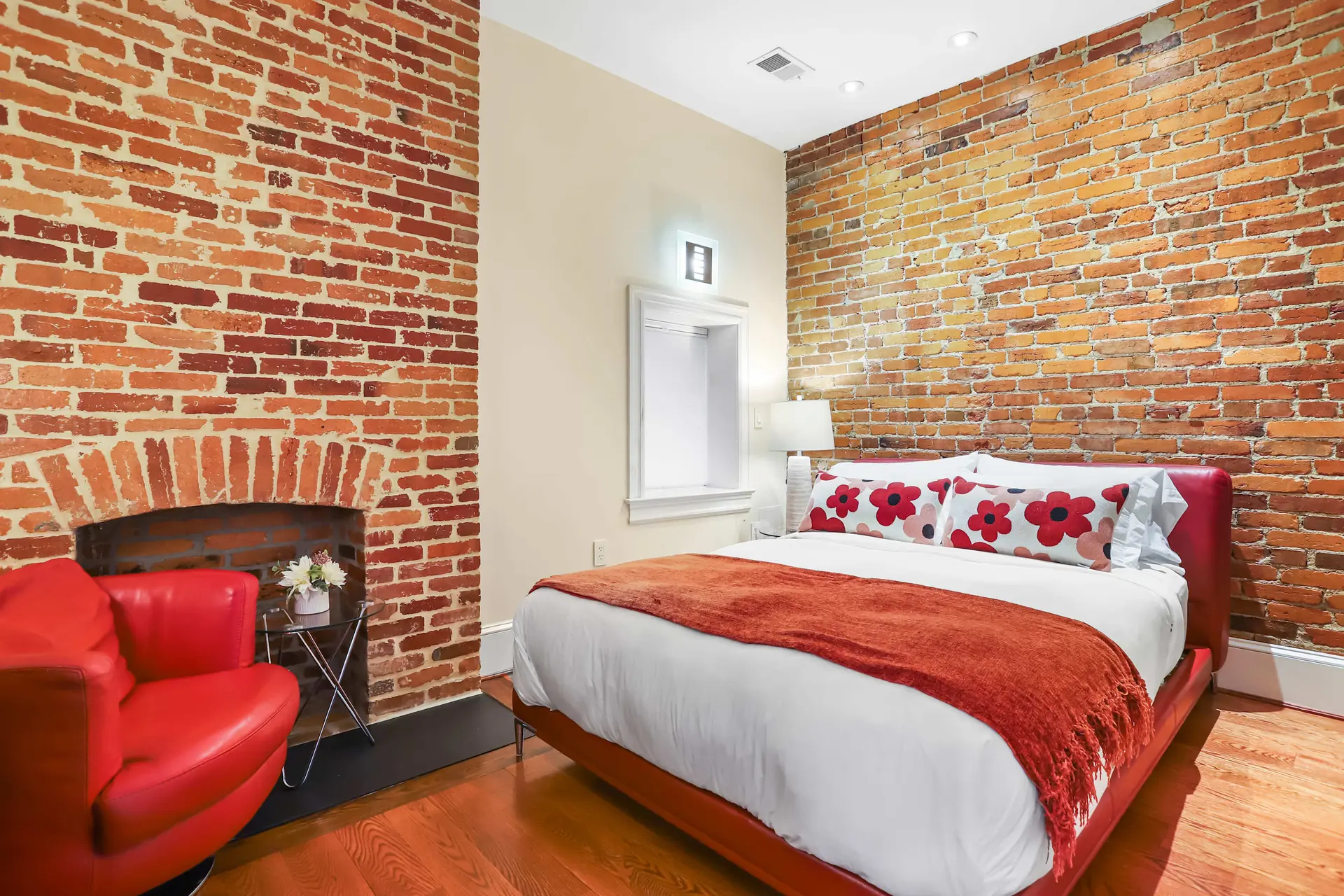 A bedroom with a red chair, a bed, and exposed brick walls.