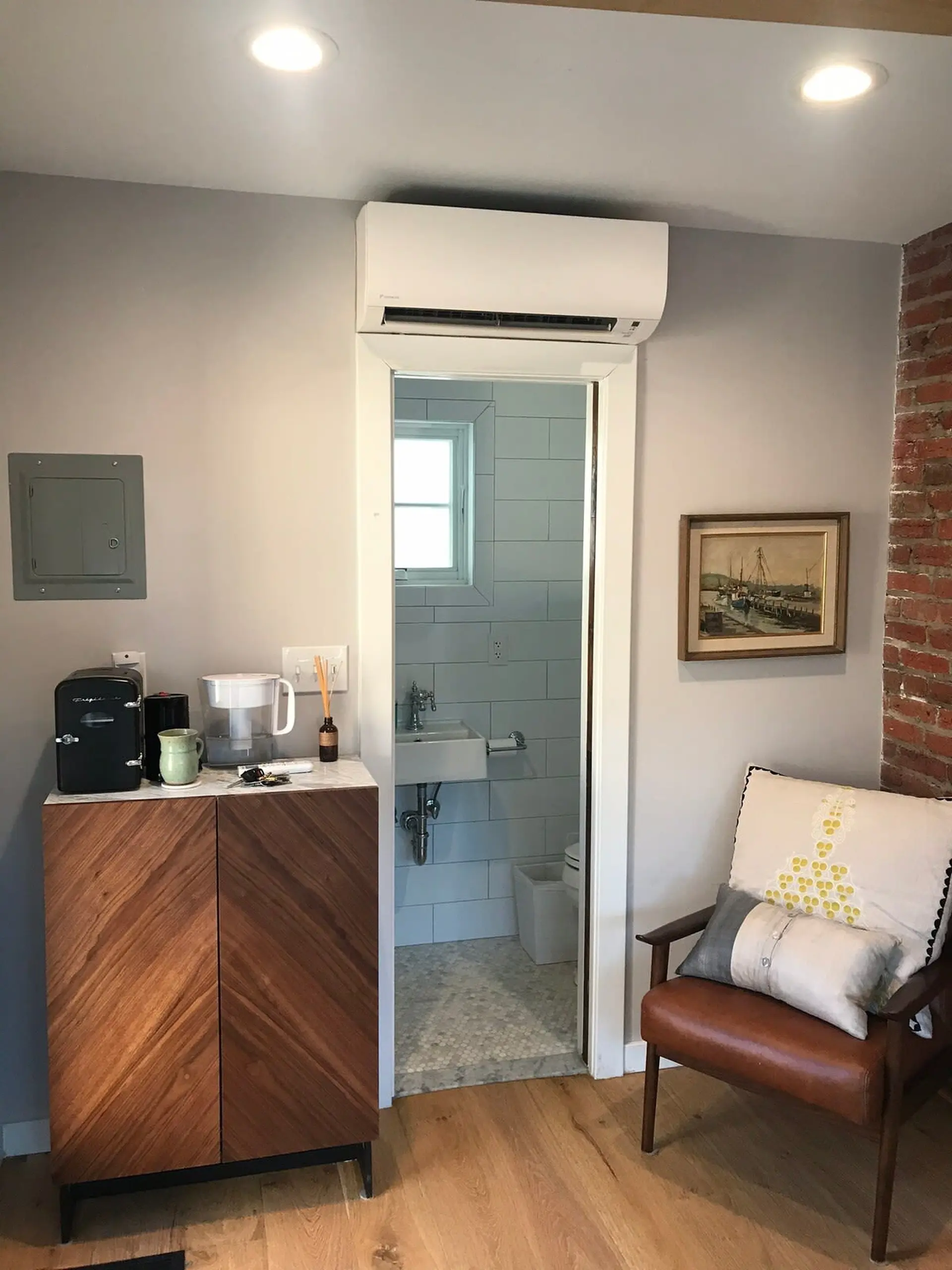 A small bathroom and sink are visible through an open doorway, with a mini-fridge and coffee maker n