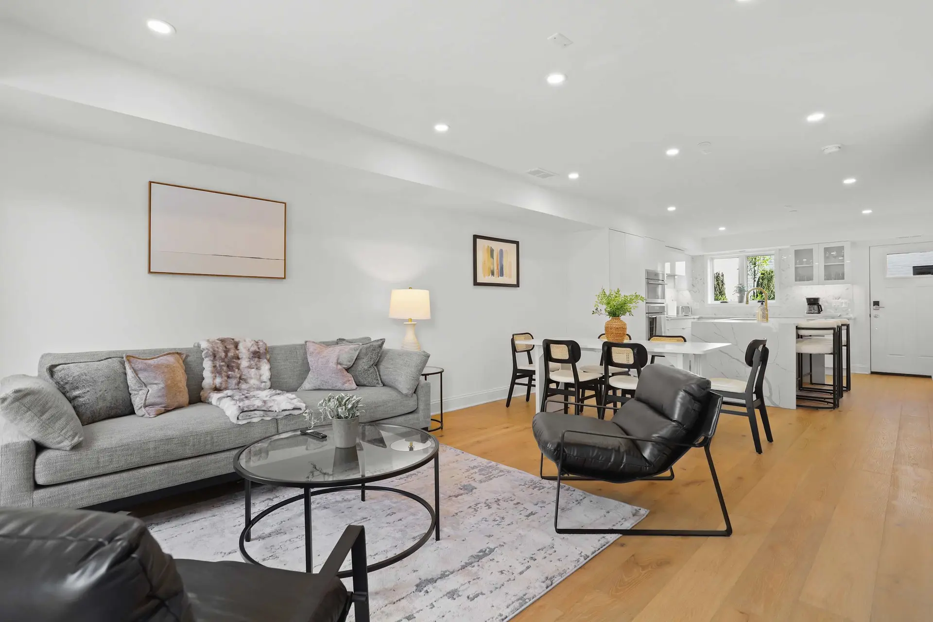 Living room with gray sofa, coffee table, chairs, and kitchen in background.