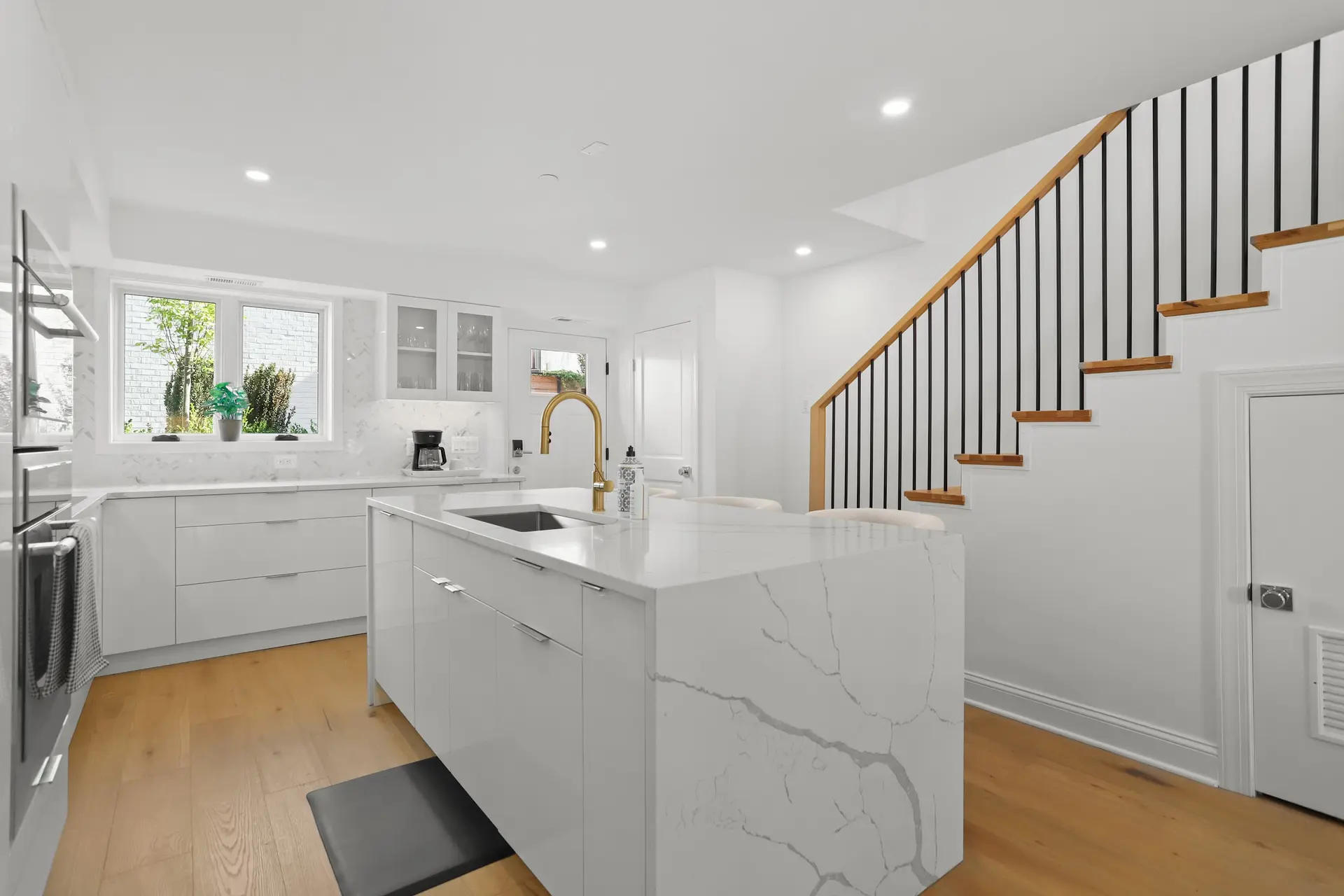 A modern kitchen with white cabinets, a marble island, and a brass faucet.