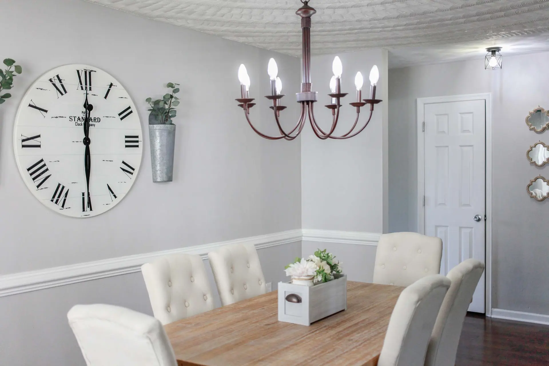 A dining room with a wooden table, tufted chairs, and a large round clock.