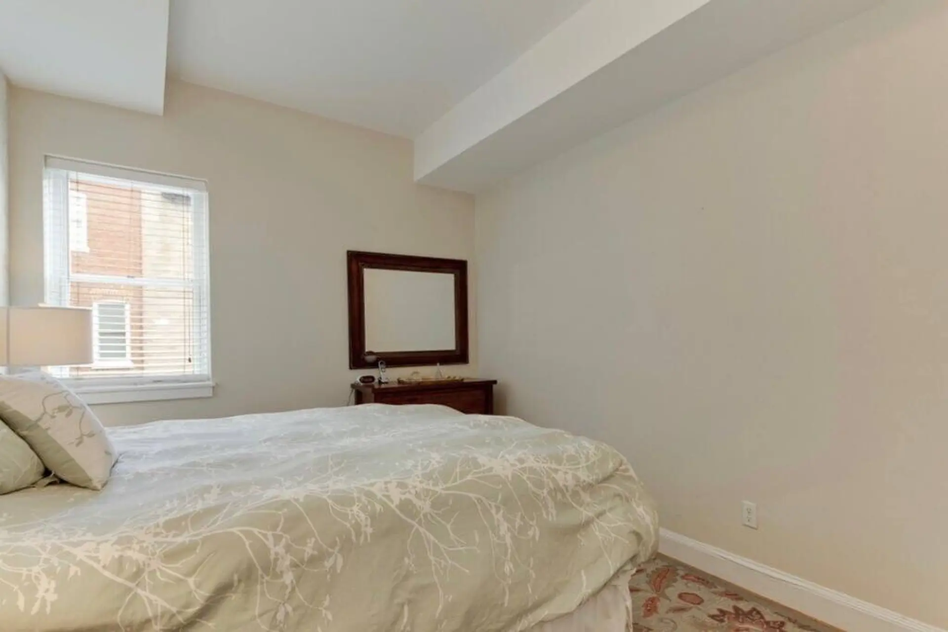A bedroom with a bed, mirror, dresser, and window.
