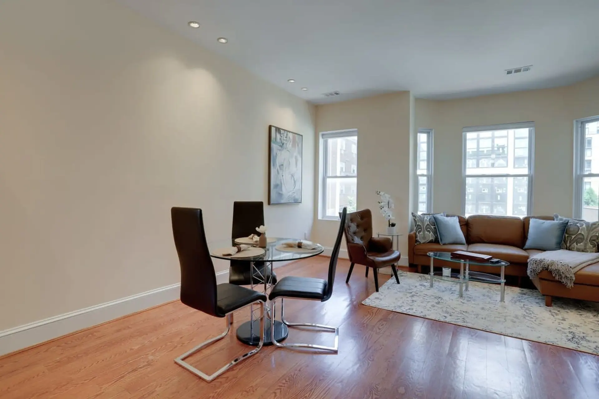 A spacious living and dining area with a sectional sofa, glass table and chairs, and hardwood floors