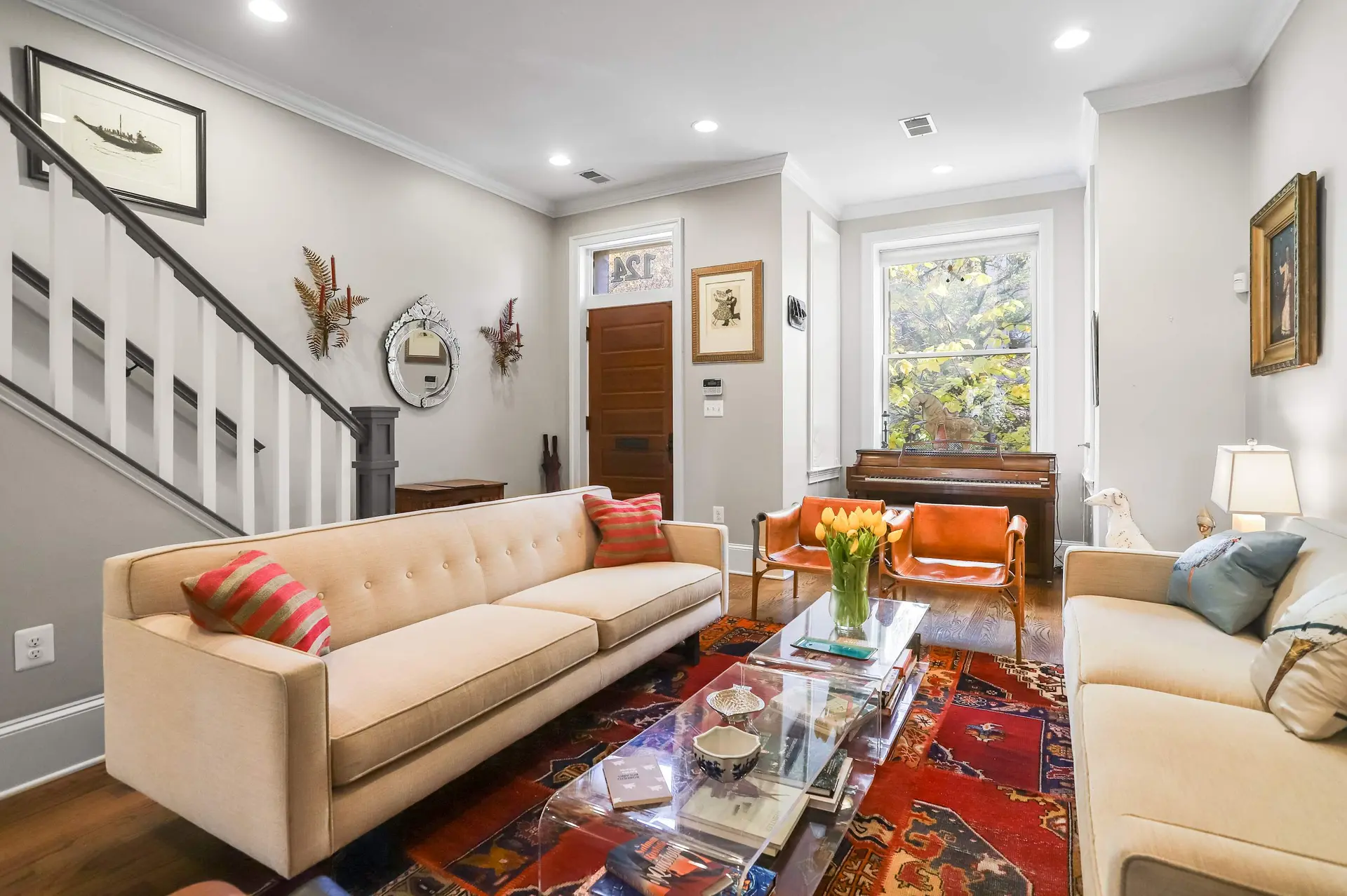 A spacious living room with a piano, two sofas, orange chairs, and a rug.