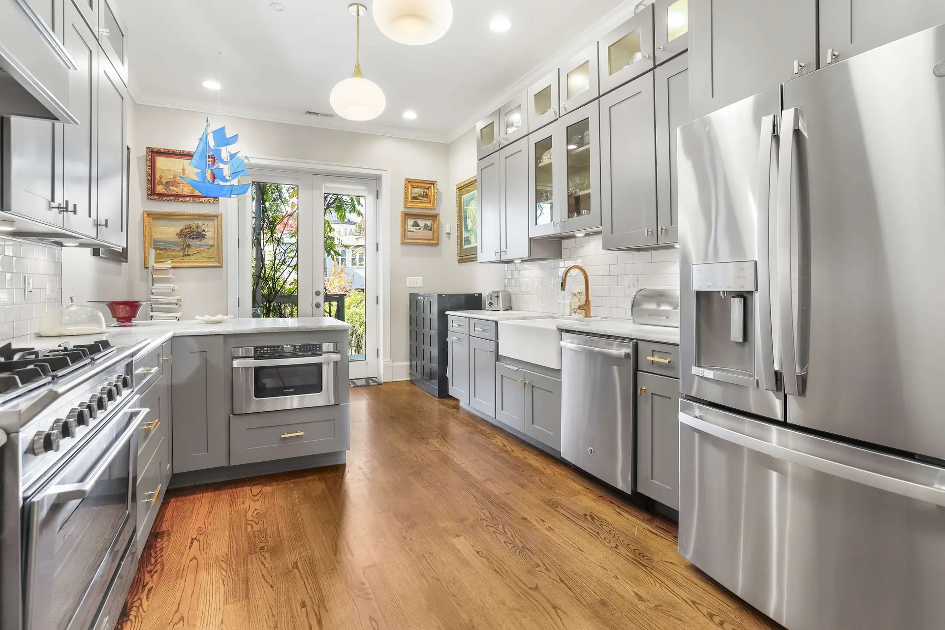 A modern kitchen with stainless steel appliances, grey cabinets, and wooden floors.