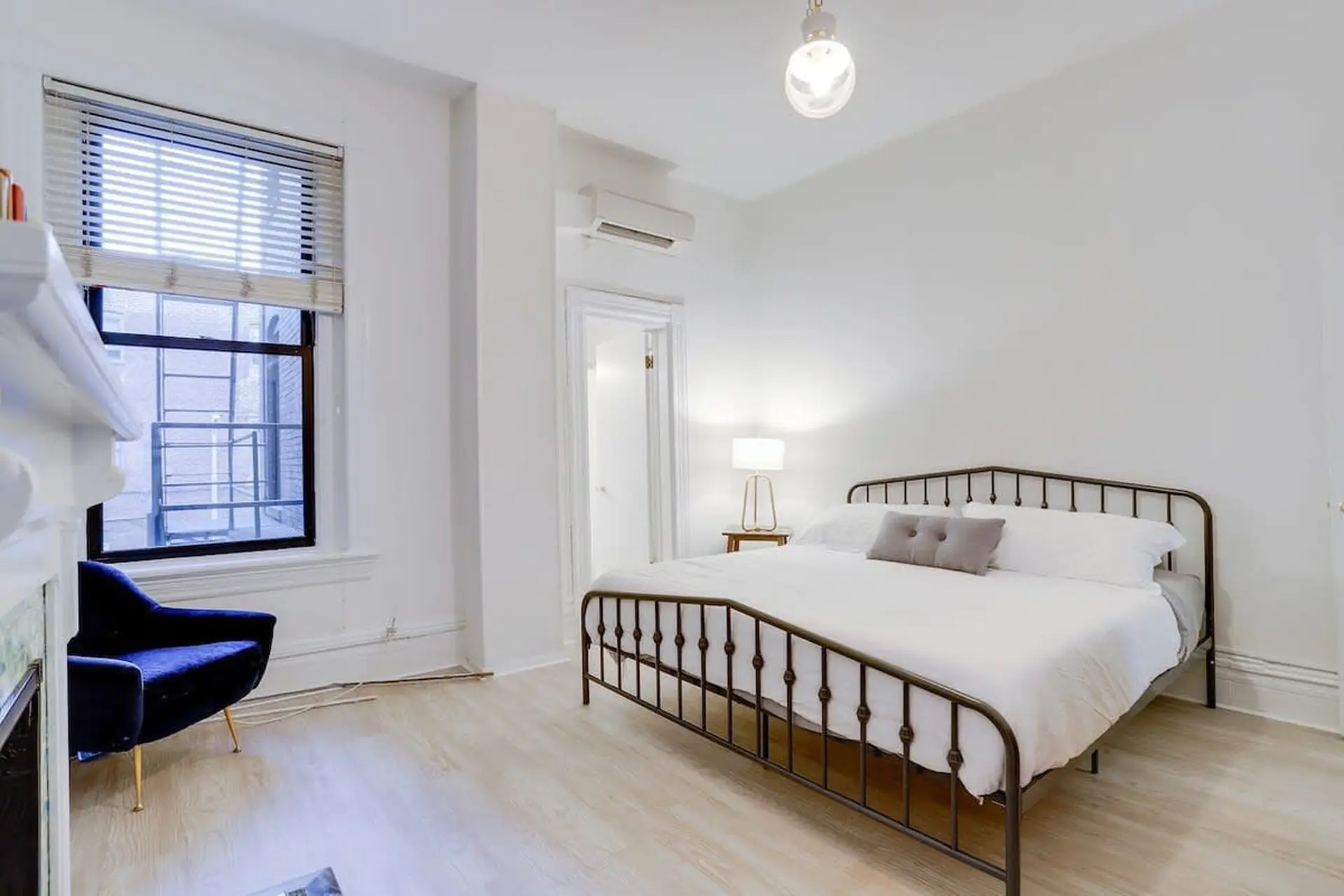 A bed with a dark metal frame and white bedding sits in a brightly lit room.