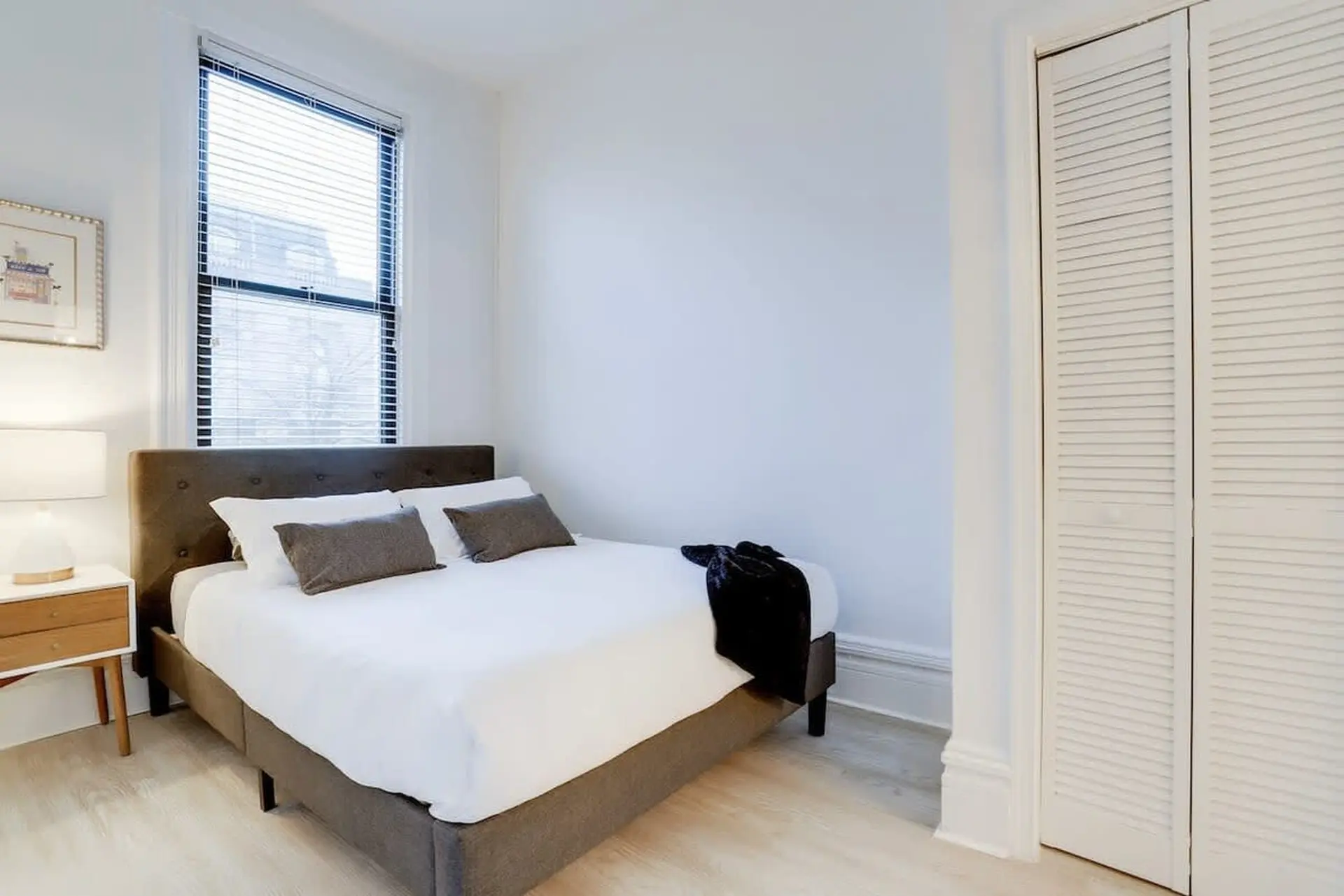 A bedroom with a bed, nightstand, window, and closet.