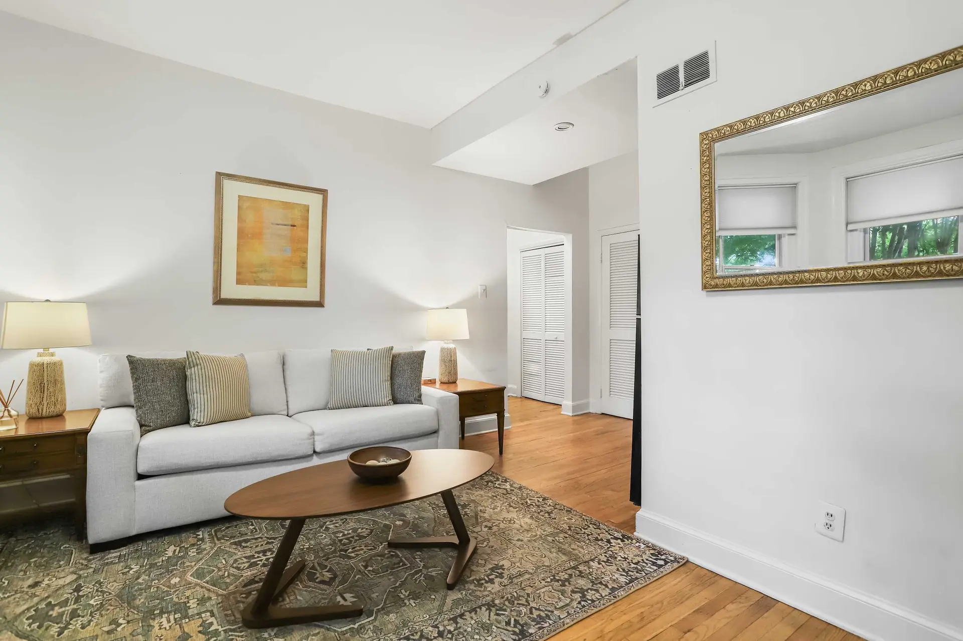 A stylish living room with a neutral couch, wooden coffee table, and a ornate gold mirror.