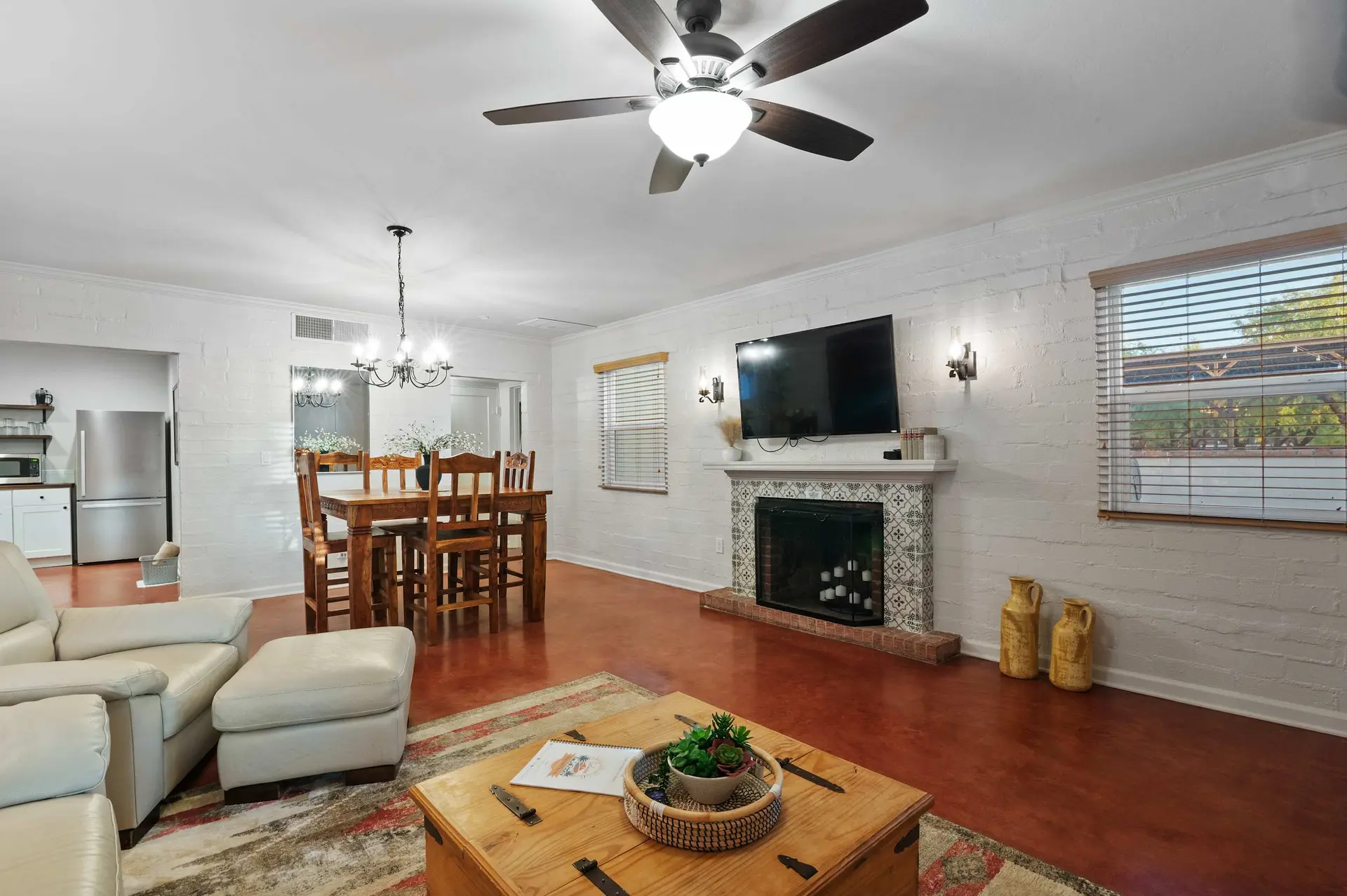 A spacious, white-brick living room with a dining area, fireplace, and a large TV.