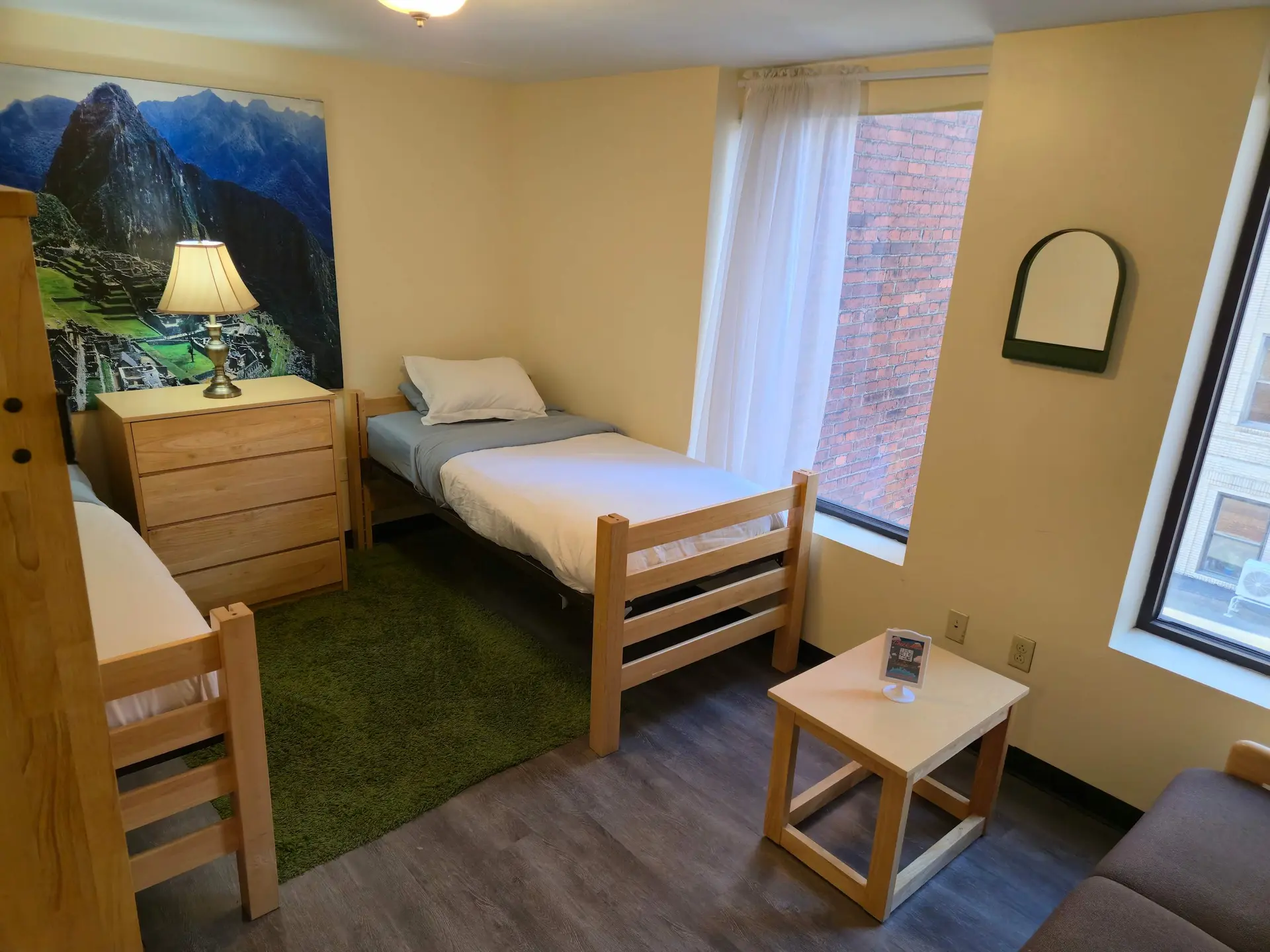 A dorm room with two beds, a dresser, and a small table.