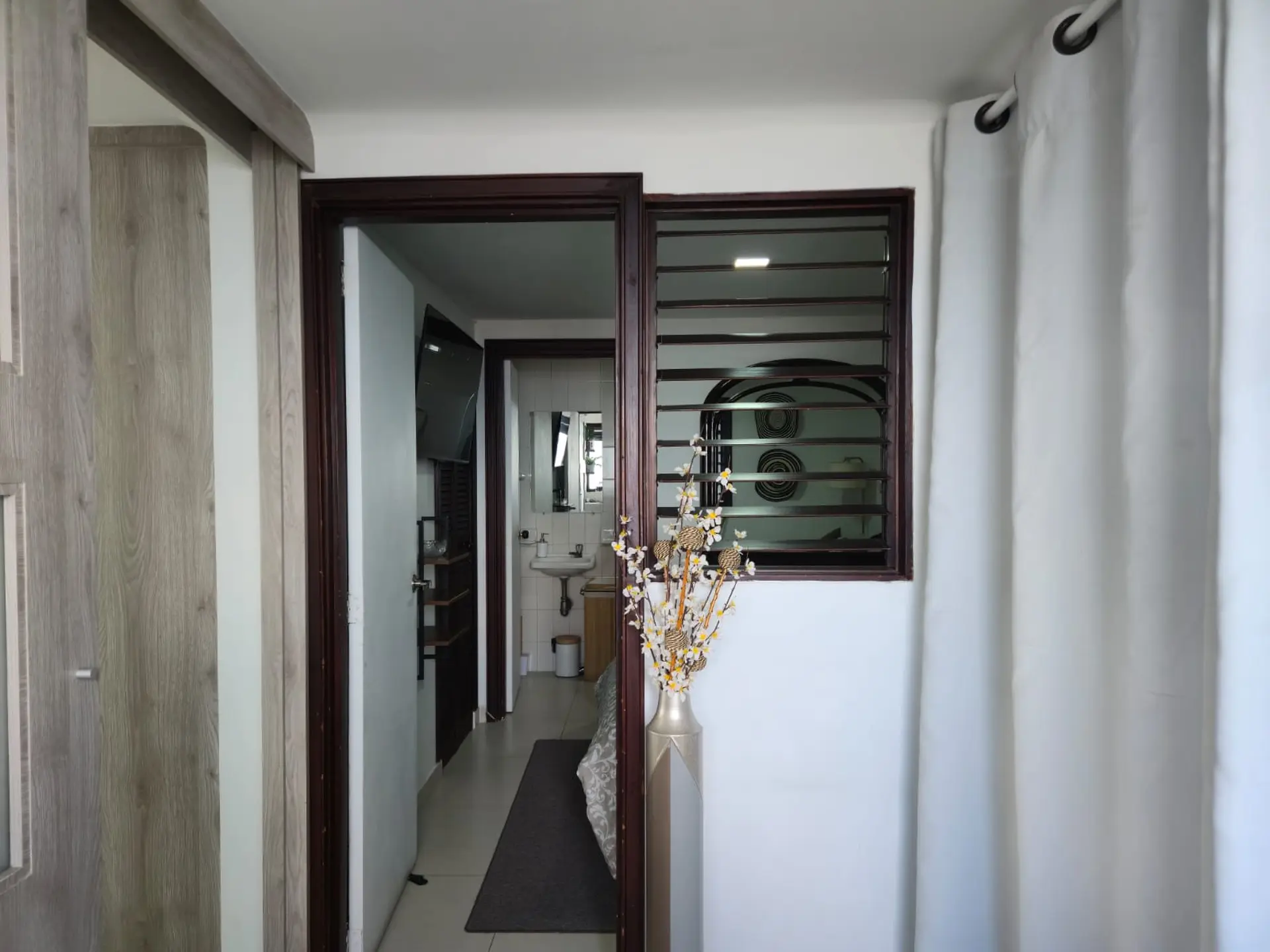 White curtains hang next to a window with horizontal blinds, on a white wall.