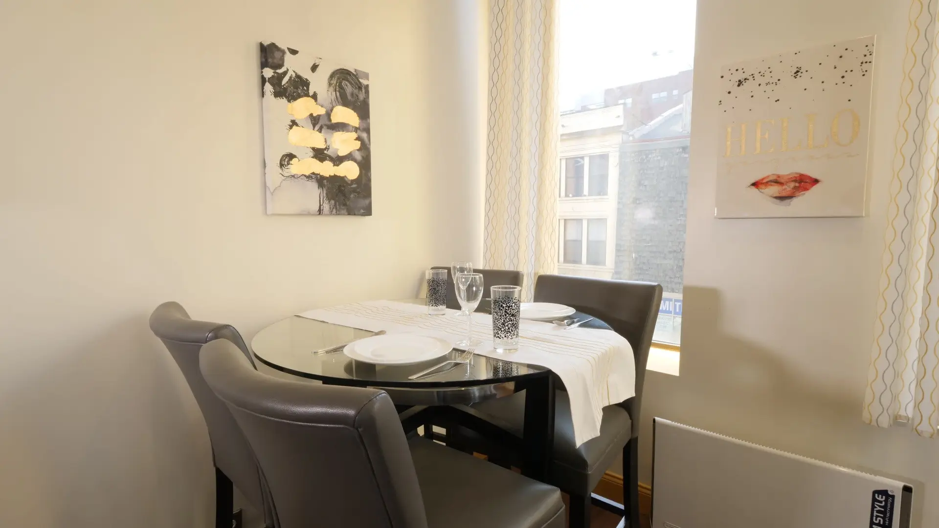 A round glass dining table is set for two with white plates, cutlery, and glasses.