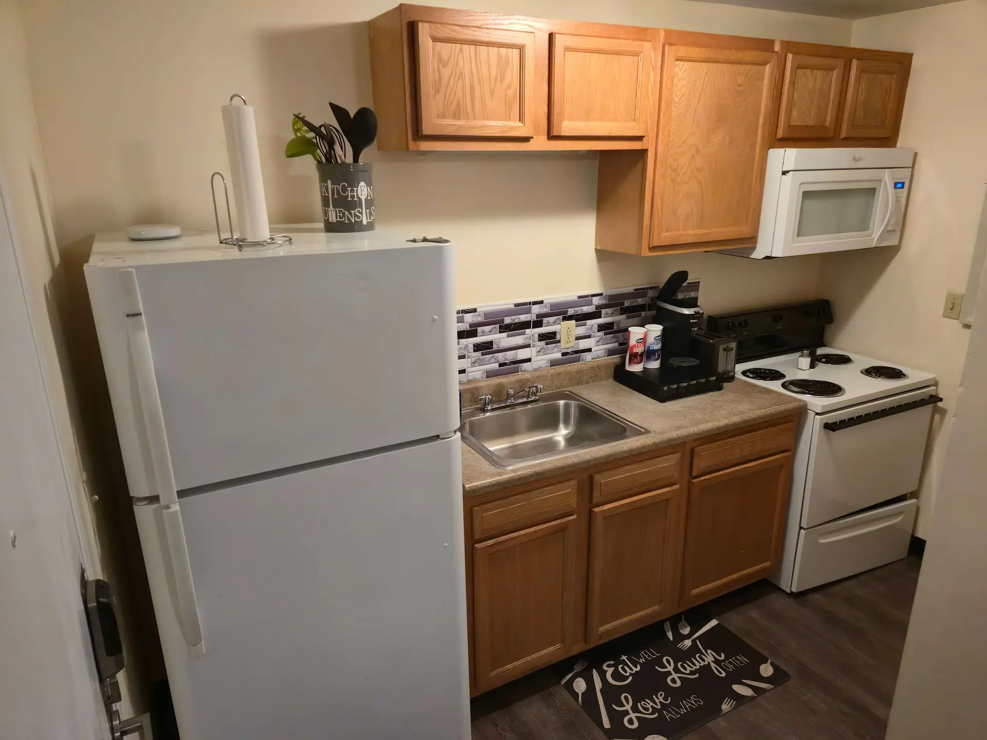 A small kitchen with a white refrigerator, sink, stove, and microwave.