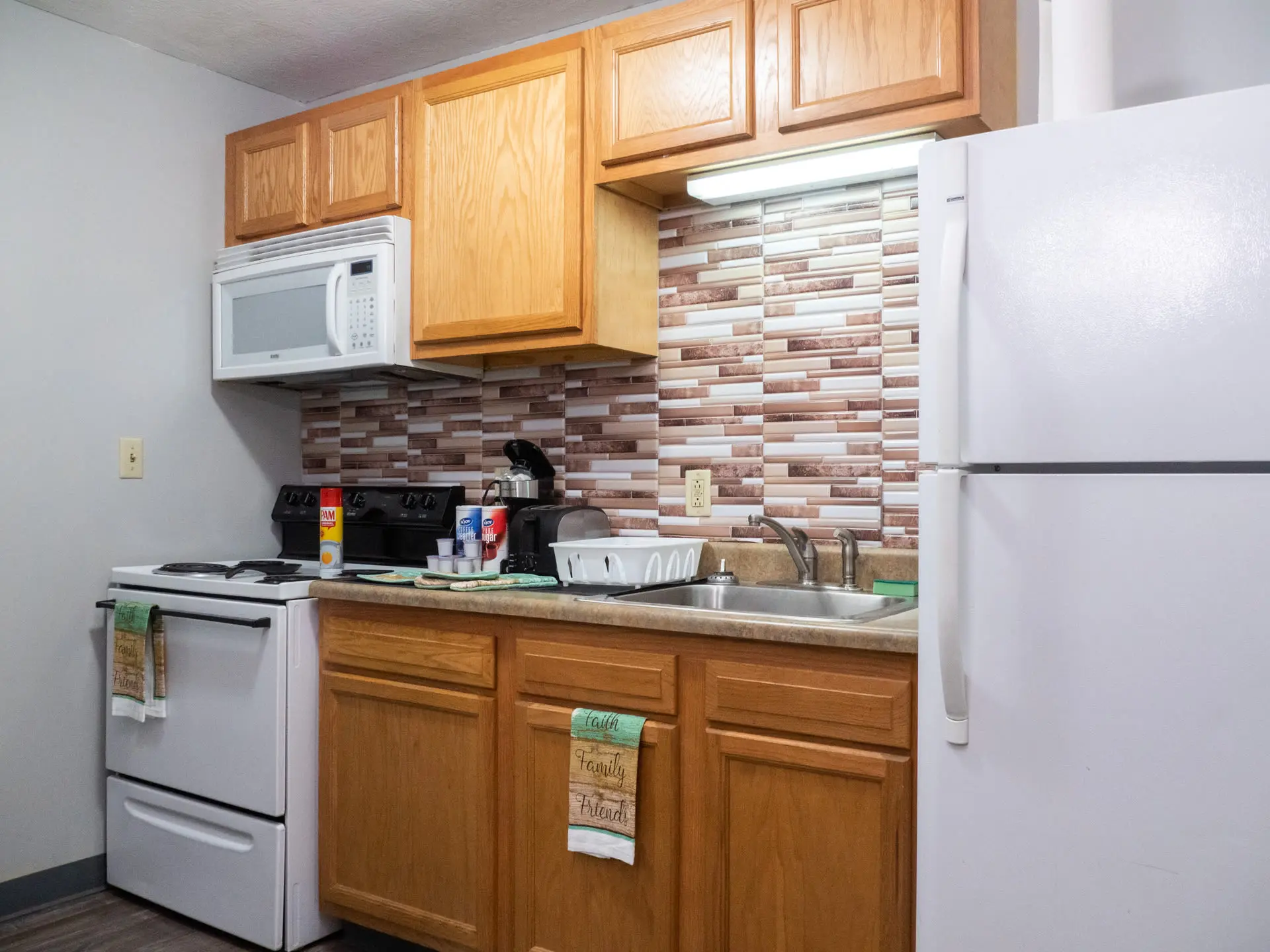 A white refrigerator is next to a kitchen sink and a wooden cabinet.