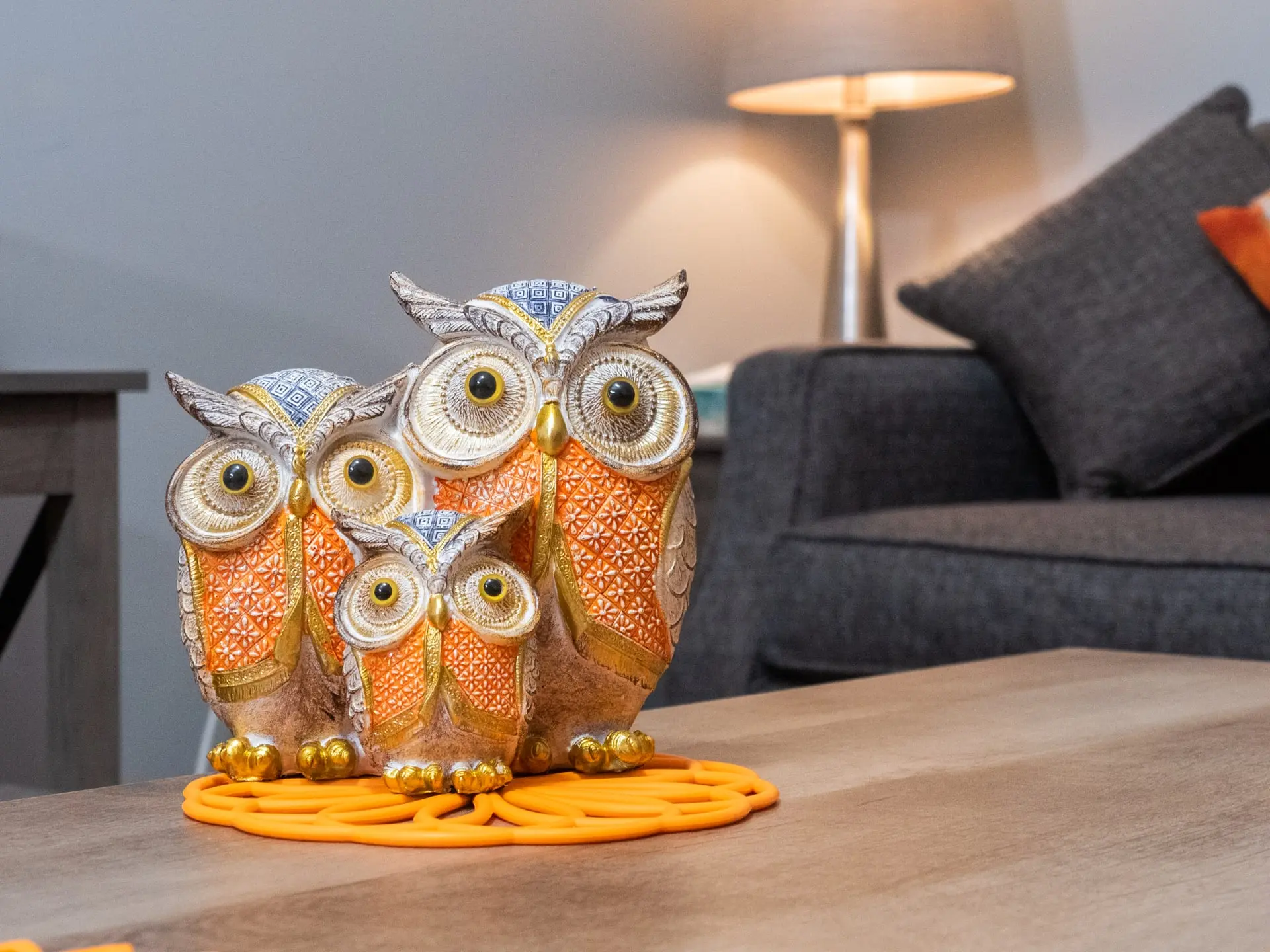 Three decorative owls with orange and gold details sit on a wooden table.