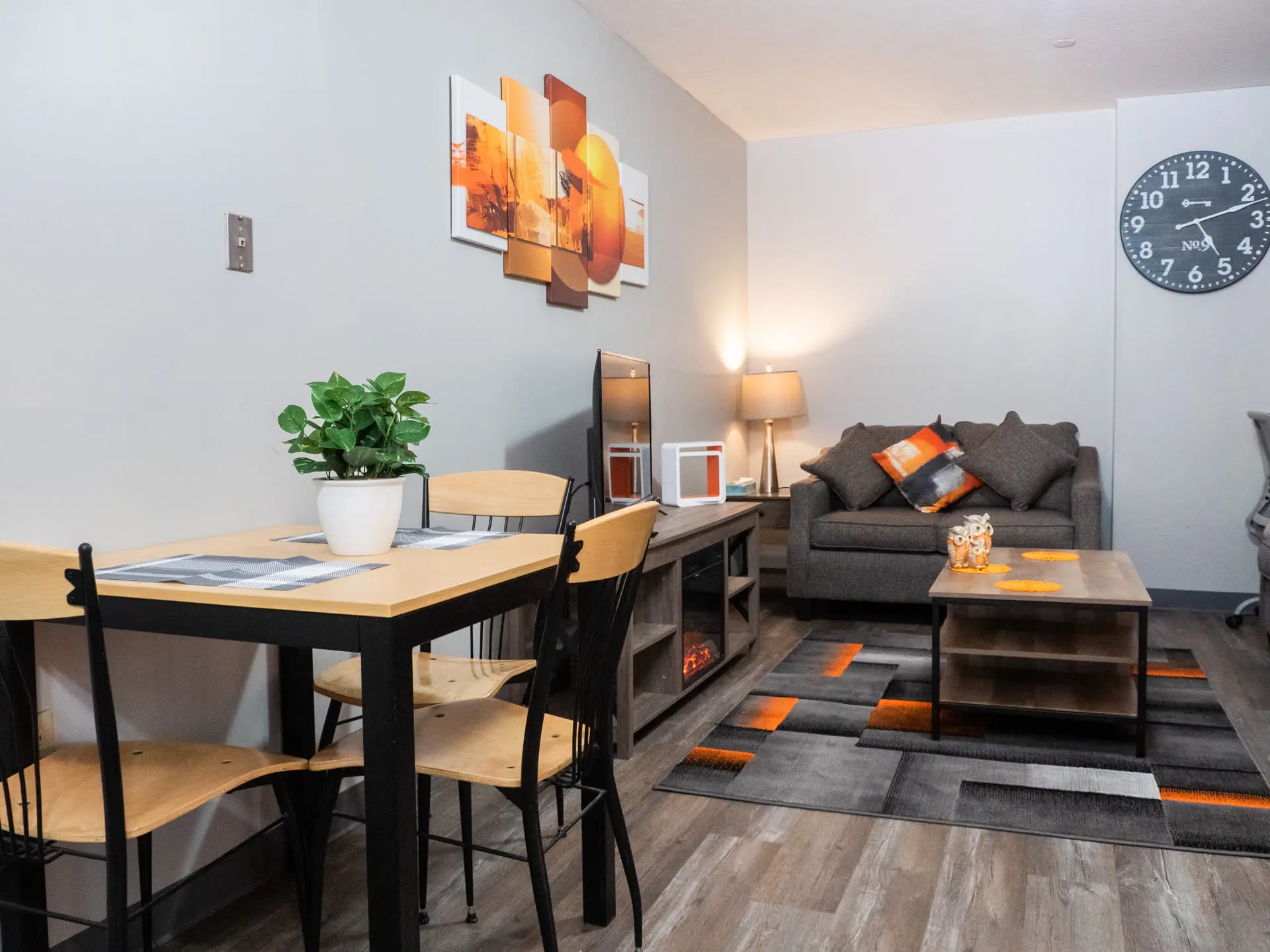 A dining set with wooden chairs sits beside a sofa with patterned pillows.
