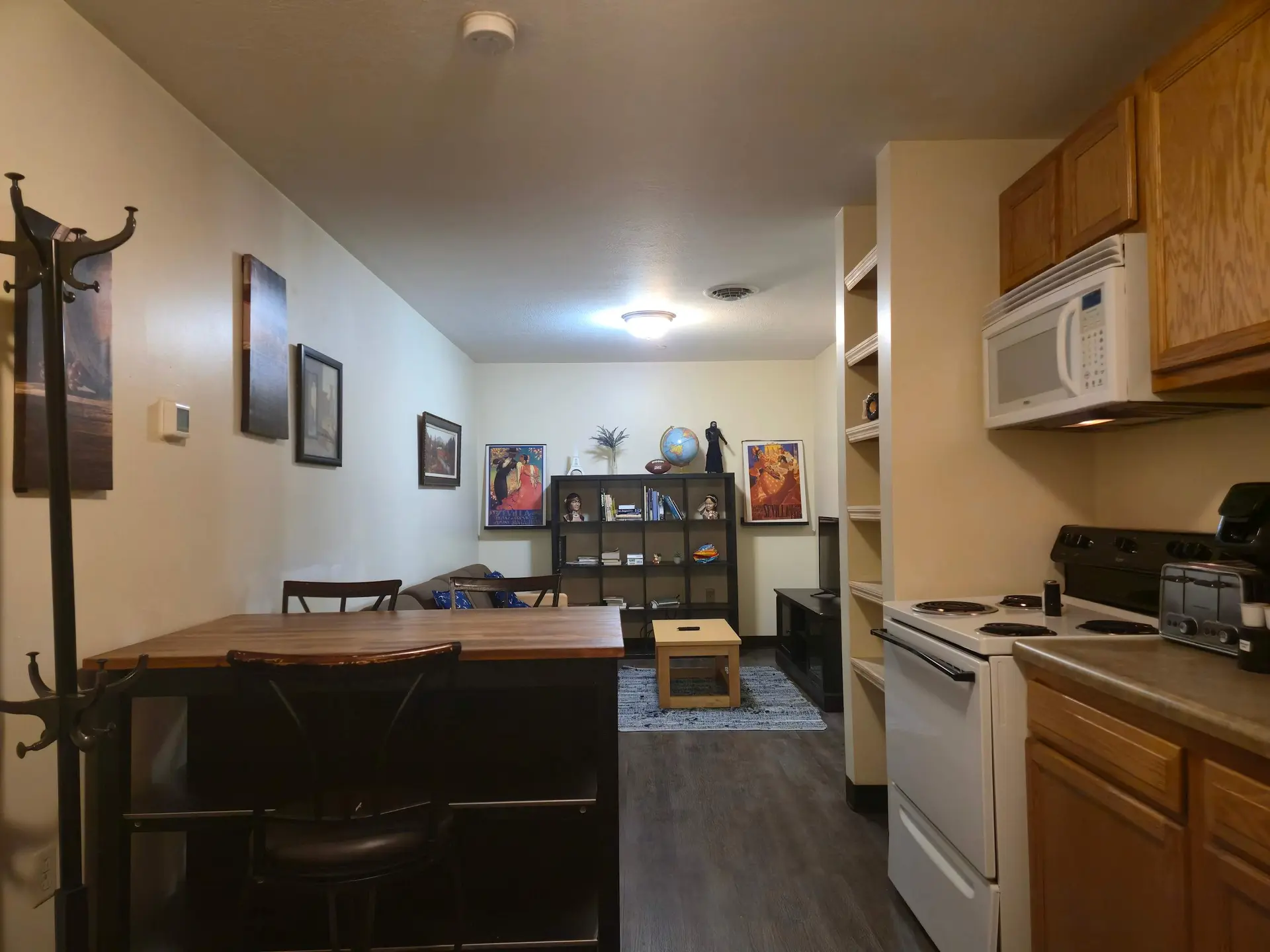 A tidy kitchen and living area with a coat rack, table, couch, bookshelves, and appliances.