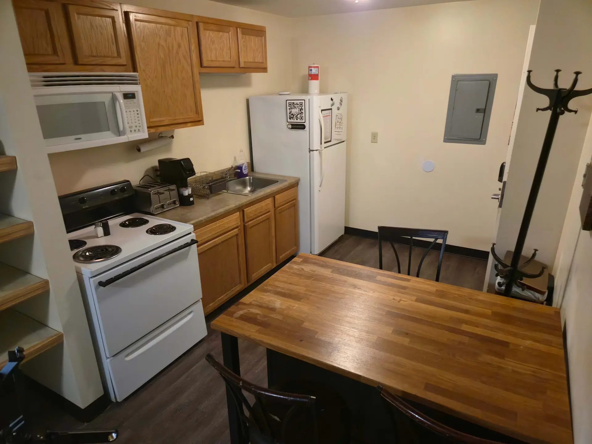 A small kitchen with a white microwave, a stove, a refrigerator, a sink, and a dining table.